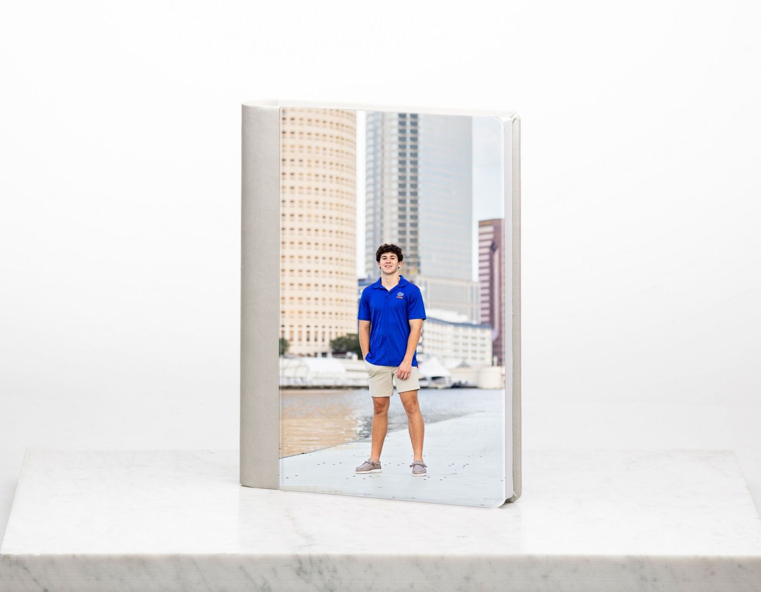 A hardcover senior portrait photo book featuring a young man in blue standing in an urban setting.