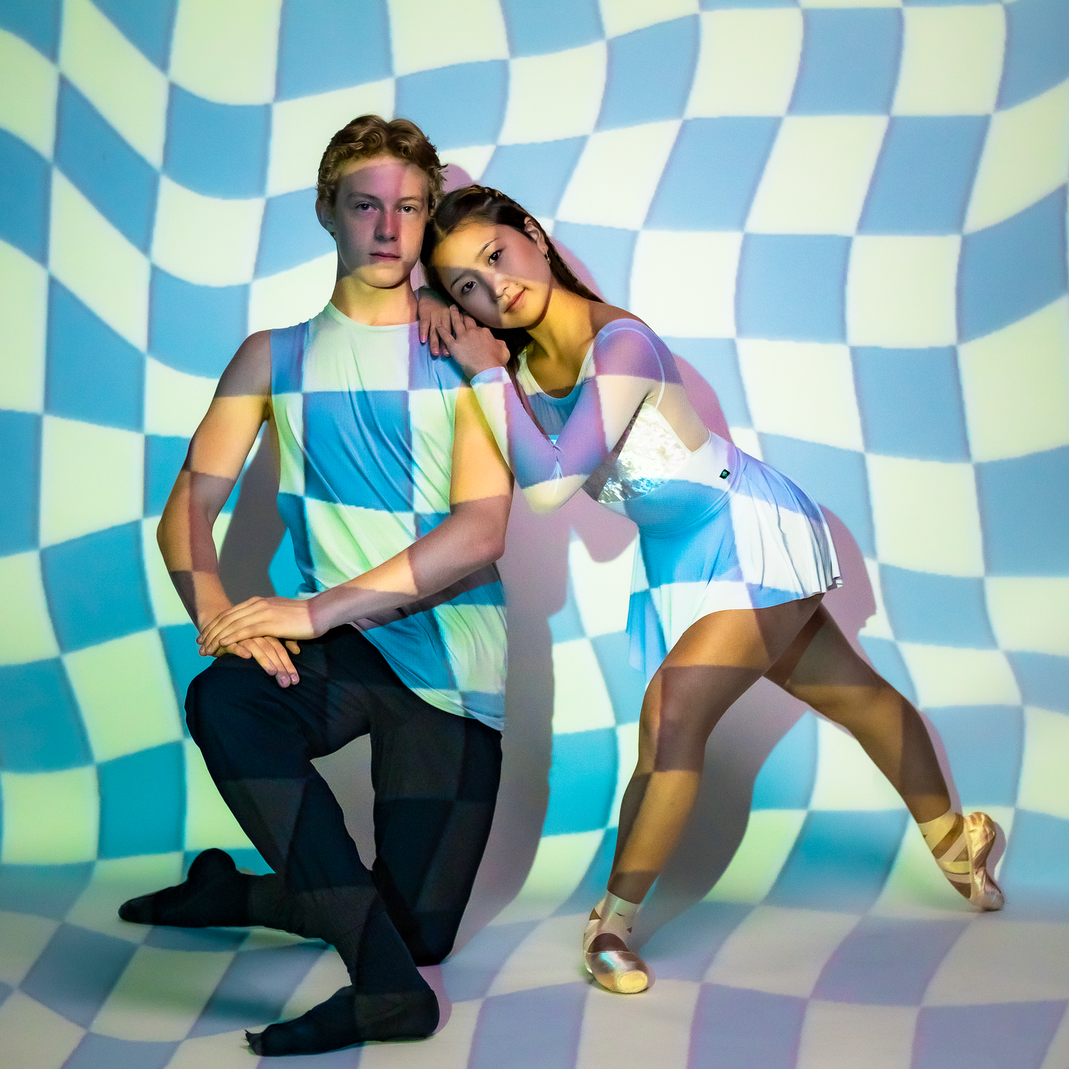 Male and female dancers pose together against blue and white checkered wavy pattern background.