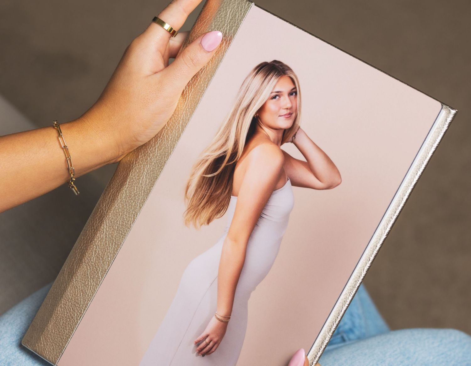 A hand holding a hardcover senior portrait photo book featuring a blonde young woman in white.