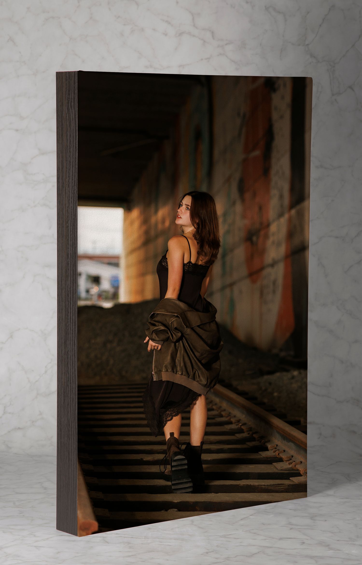 A large wood panel print of a young woman walking on railroad tracks in an urban setting.