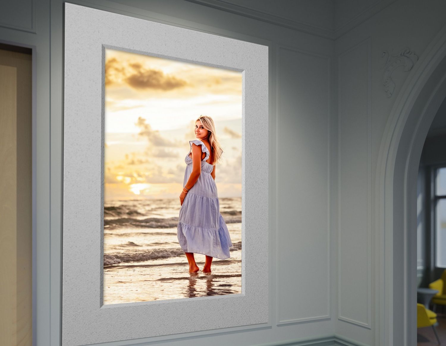 A large framed senior portrait of a blonde woman in a white dress standing on a beach at sunset.