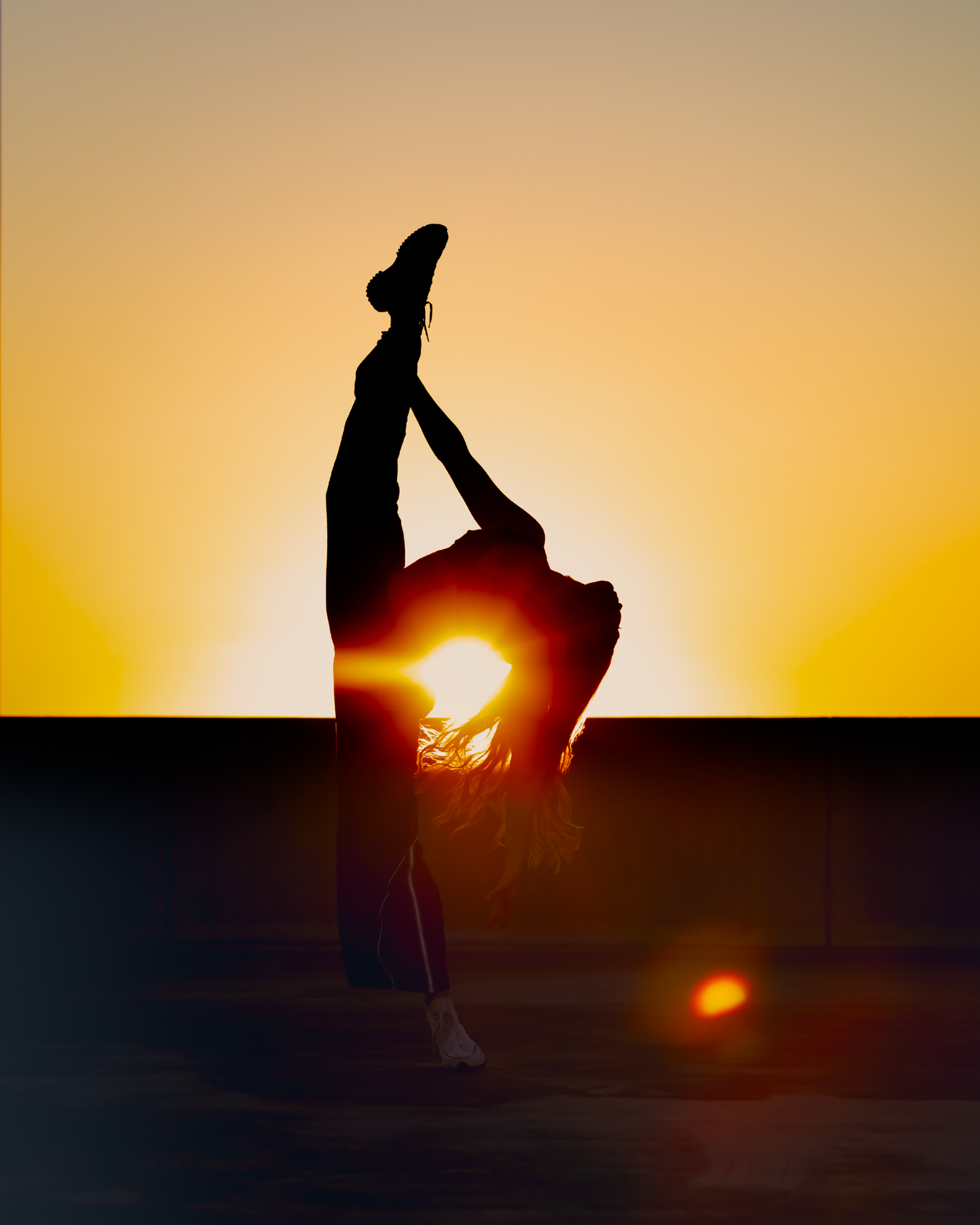 Silhouette of dancer in backbend pose with leg extended against golden sunset sky.