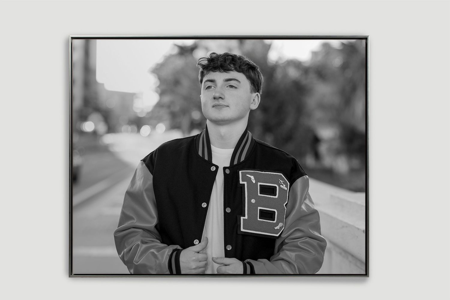 A black and white framed senior portrait of a young man wearing a varsity letterman jacket.