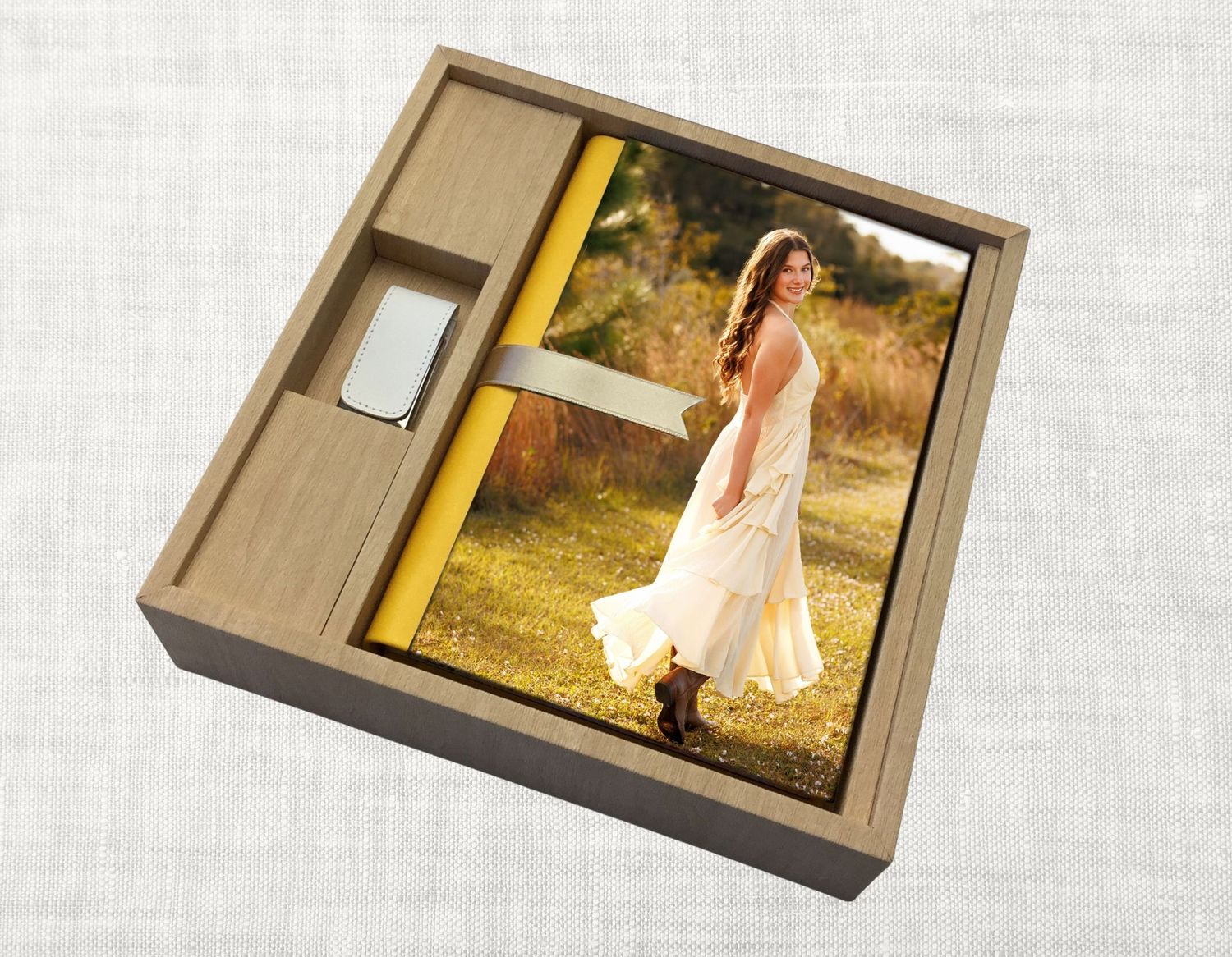 A wooden keepsake box containing senior portrait prints and a USB drive on a linen textured background.