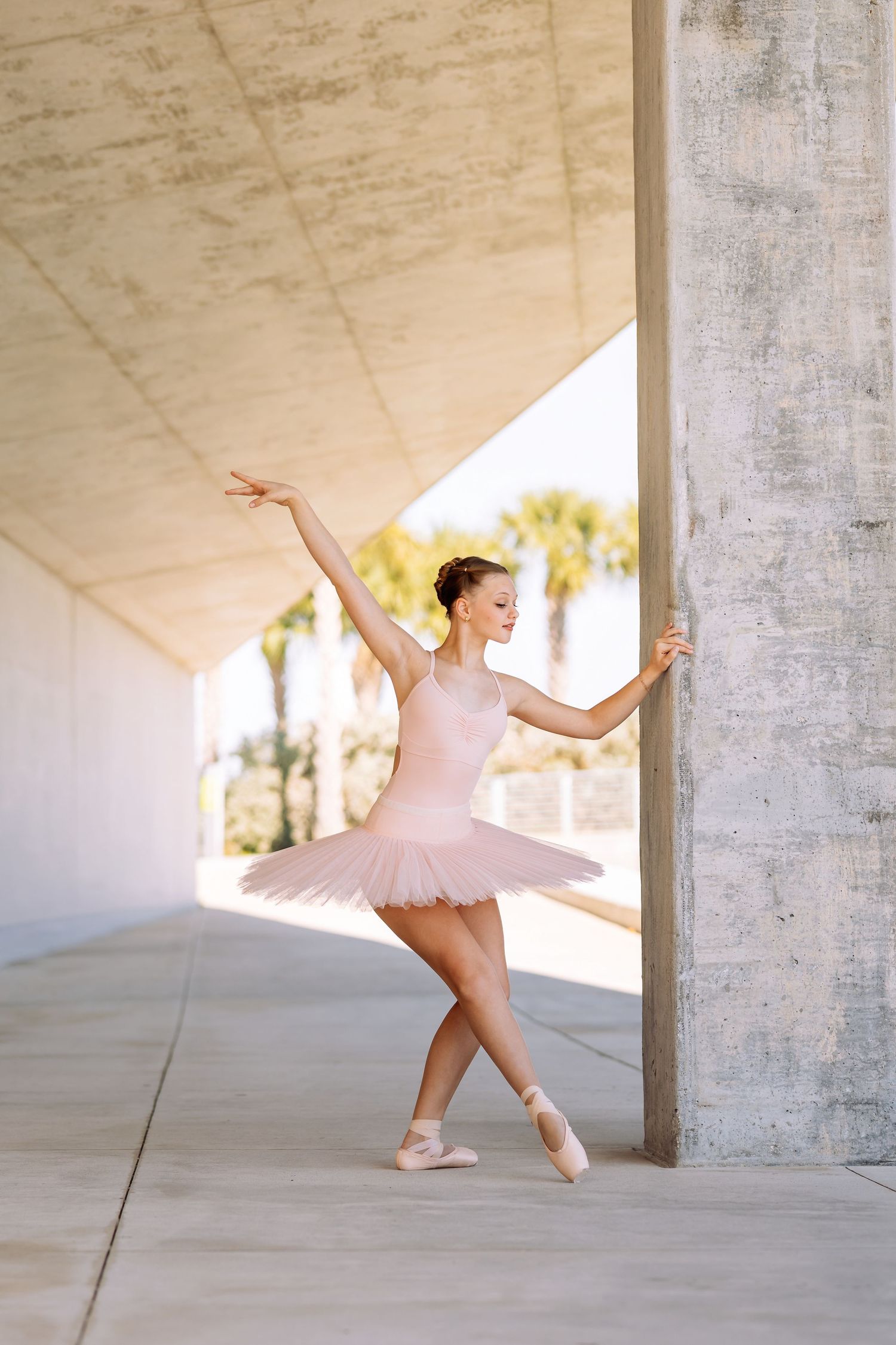 Ballerina in pink tutu poses gracefully on pointe shoes outdoors near concrete columns.