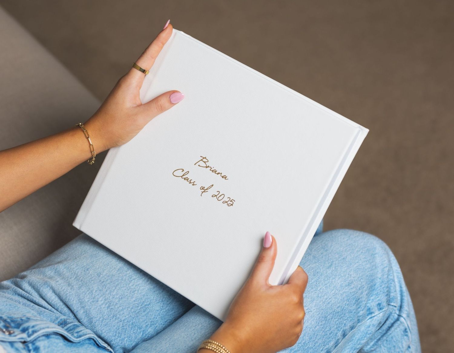 Hands holding a white personalized senior photo book inscribed with Briana Class of 2023 in gold foil lettering.