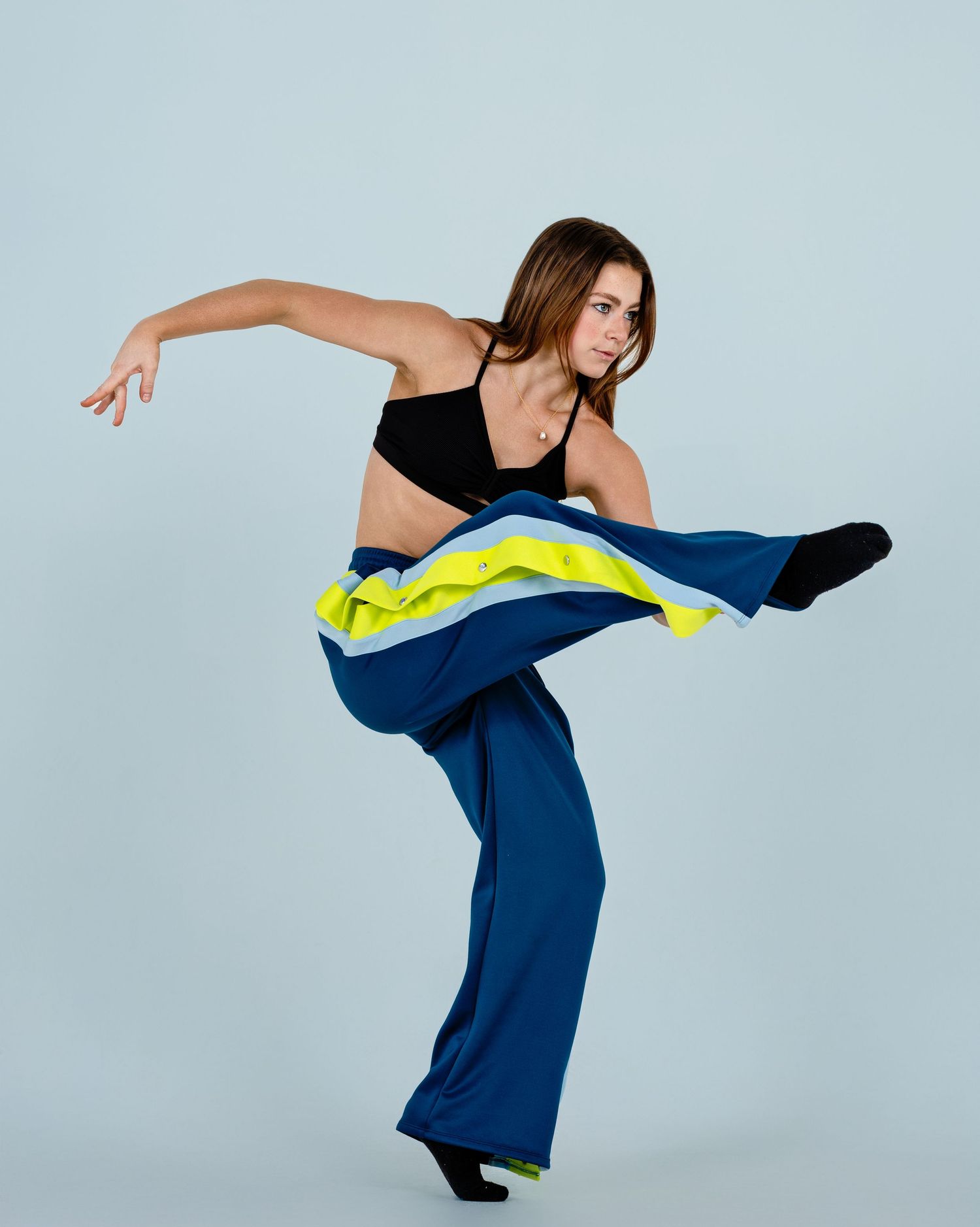 Female dancer in black crop top and blue wide-leg pants performing a high kick in studio.