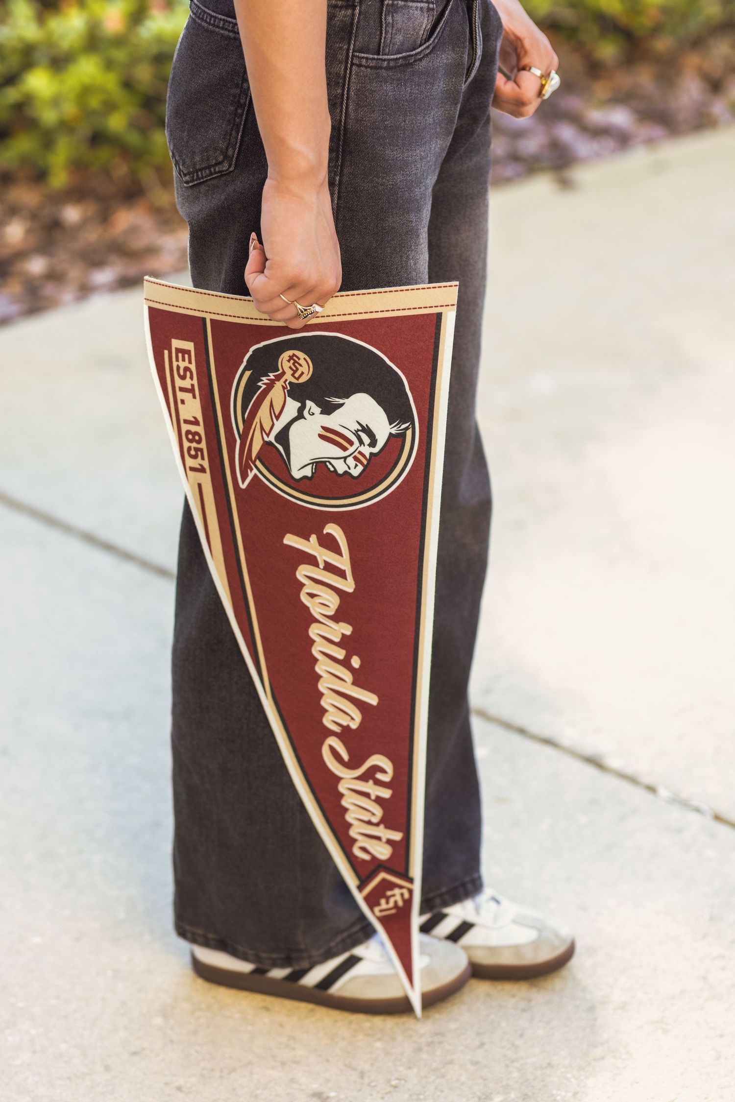 Person holding a Florida State Seminoles pennant flag, established 1851, in garnet and gold colors.