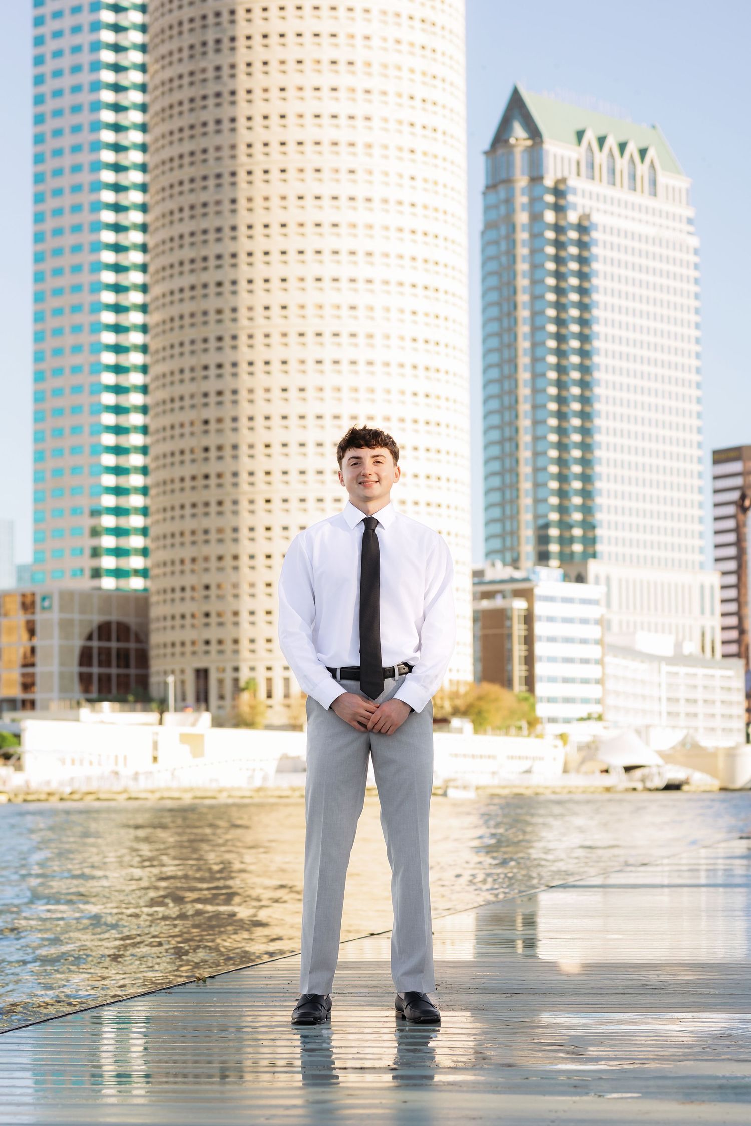 Young man in white dress shirt and tie poses confidently in front of Tampa city skyline.