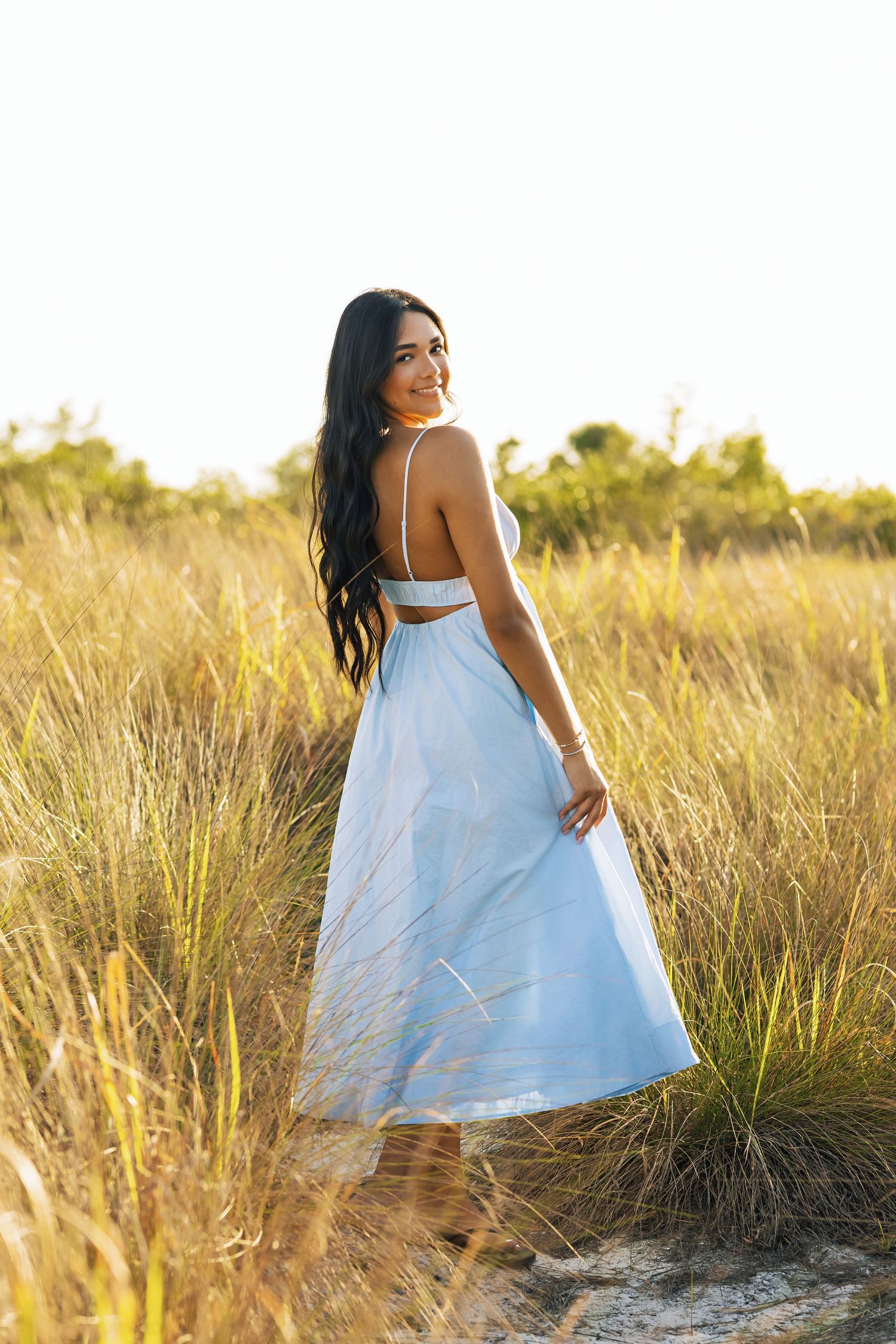 Brunette woman in white two-piece outfit standing in golden grass field during bright sunny day.