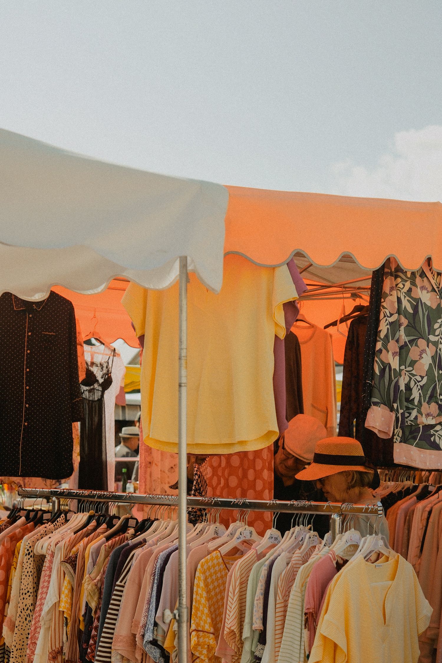 Colorful outdoor clothing market stall with yellow and floral tops on display.