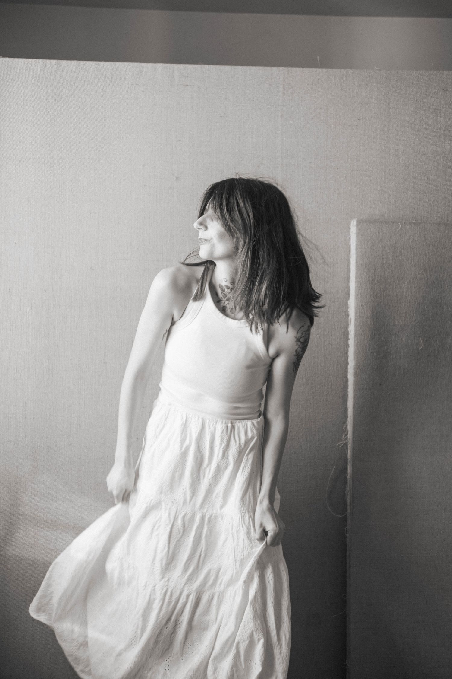 Black and white photo of a woman in a white dress with flowing skirt, hair blowing, looking away.