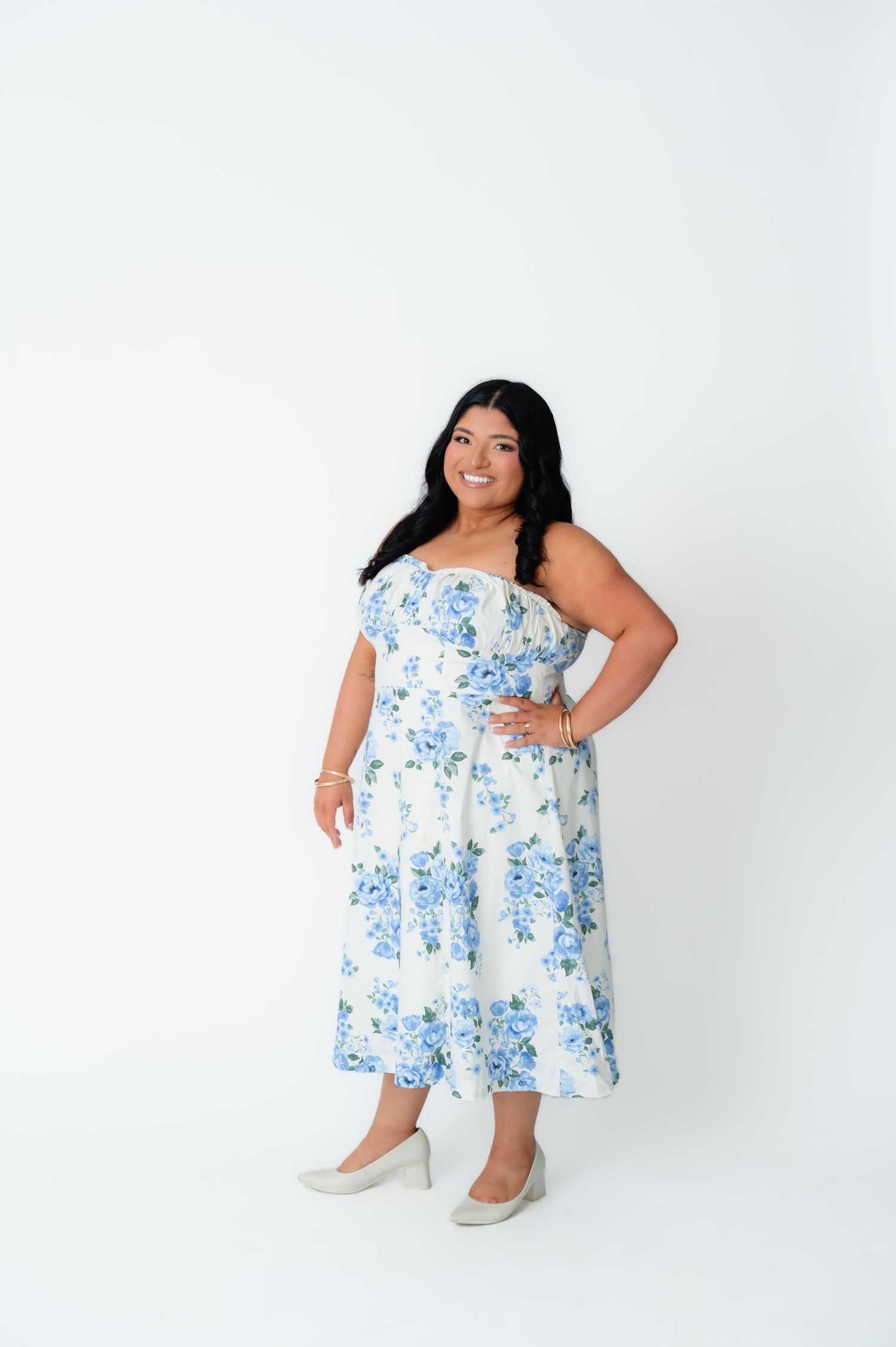 Woman in white floral midi dress with blue flowers, strapless style, posing confidently on white background.