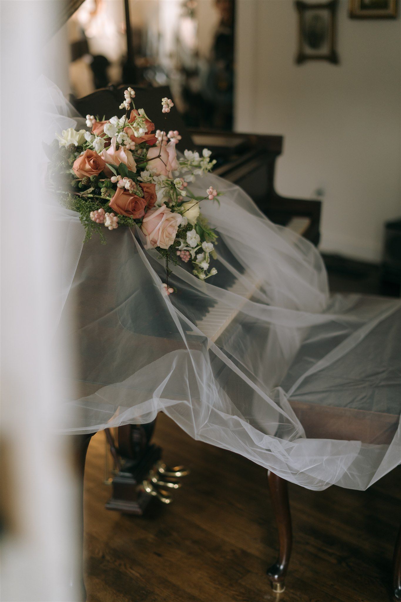 Elegant bridal bouquet of pink roses resting on a piano draped with flowing white tulle veil.