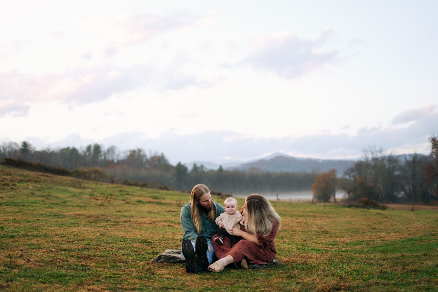 Two women sitting on a grassy hillside with a baby and mountain lake view.