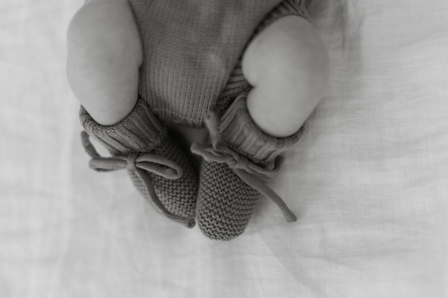 Close-up black and white photo of a newborn babys tiny feet wearing knit booties.