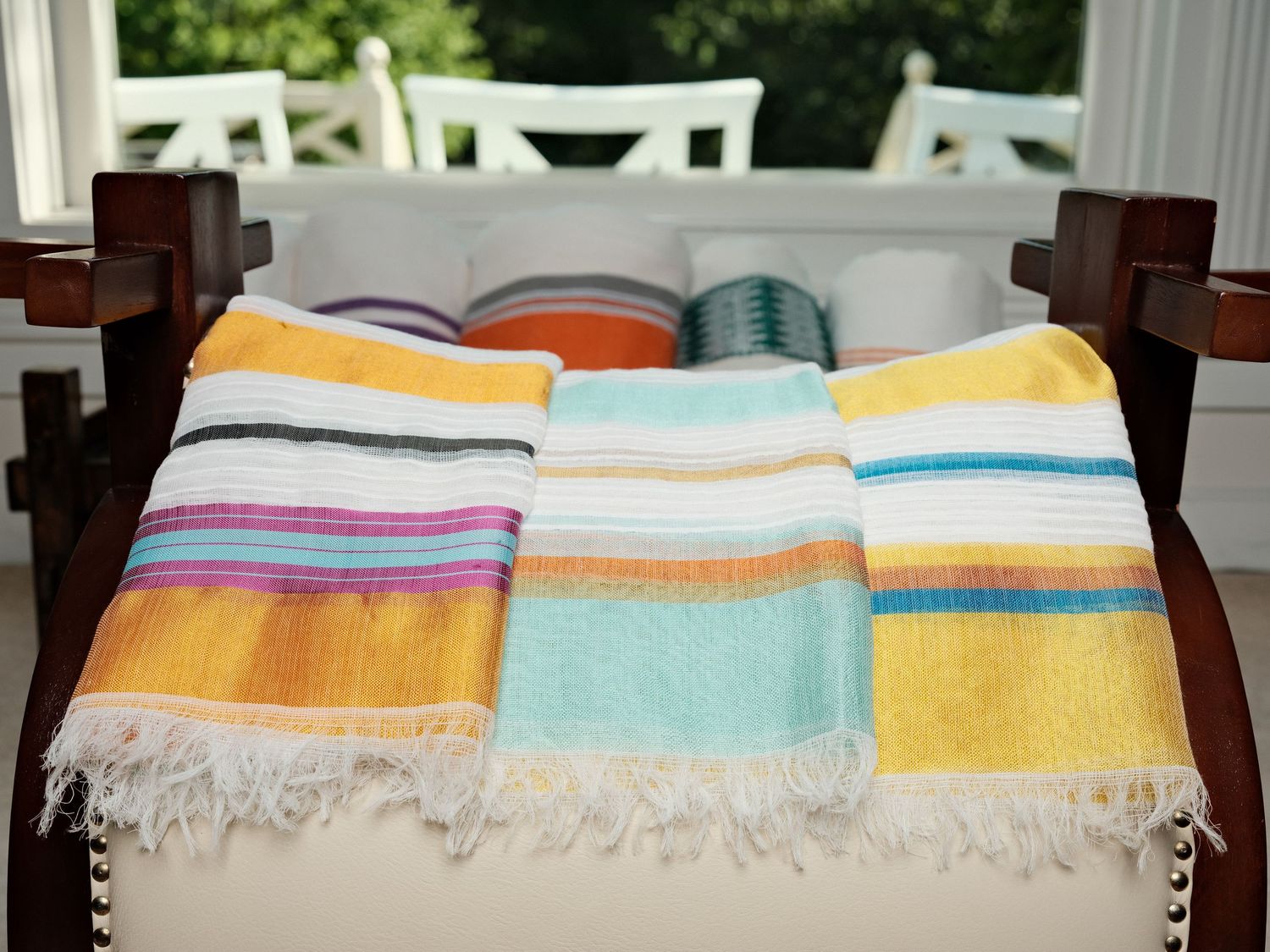 Colorful striped Turkish towels with fringe draped over a white chair, featuring yellow, teal, and multicolor designs.