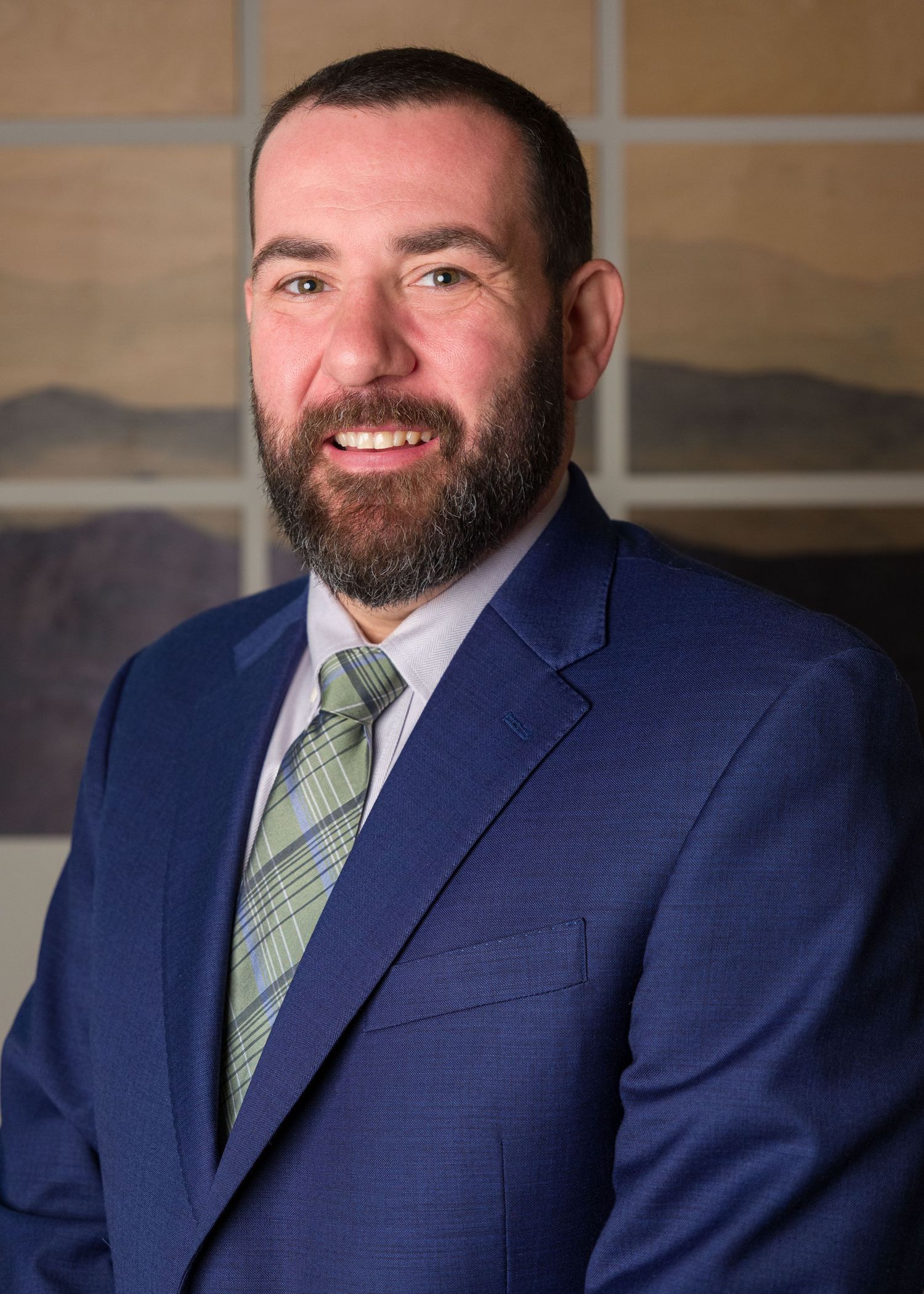 Professional man in blue suit and green tie with beard smiling in a formal business portrait photo.