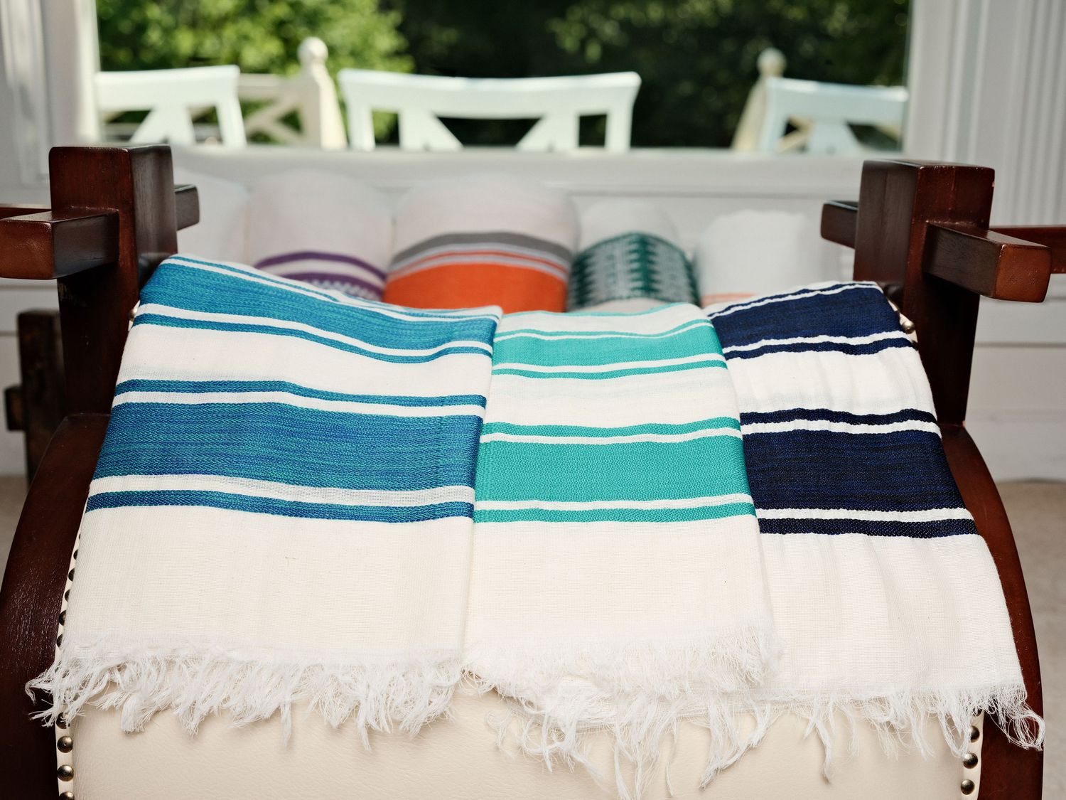 Three striped Turkish cotton towels in teal, turquoise, and navy with white fringe draped over a wooden chair.