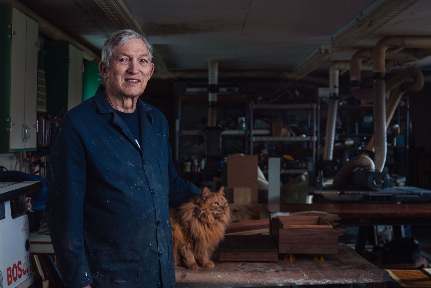 Environmental portrait of a man standing in a workshop with a cat in the background