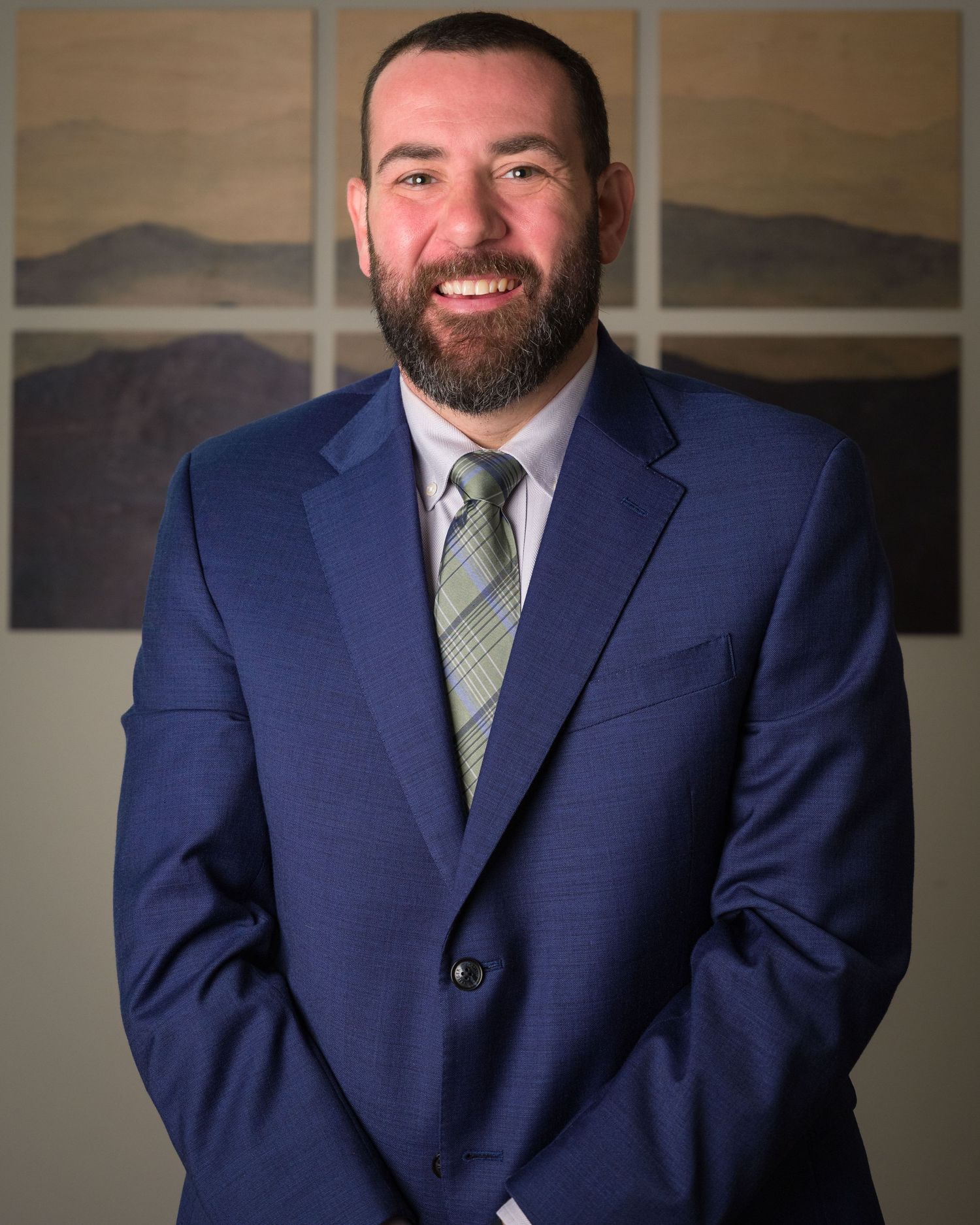 Professional man in navy blue suit and striped tie smiling confidently in a formal portrait setting.