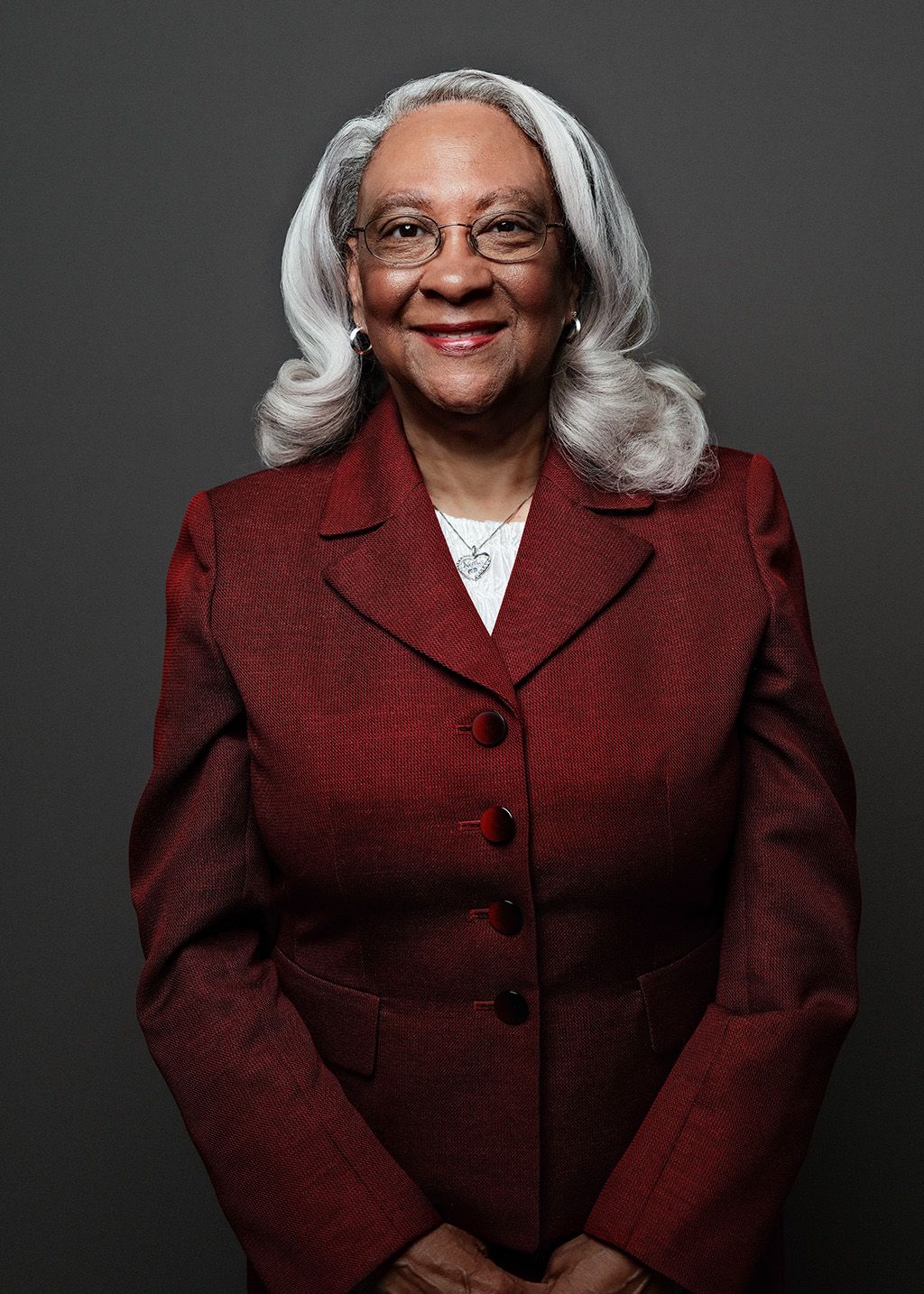Professional headshot of a woman in a burgundy blazer on a gray background