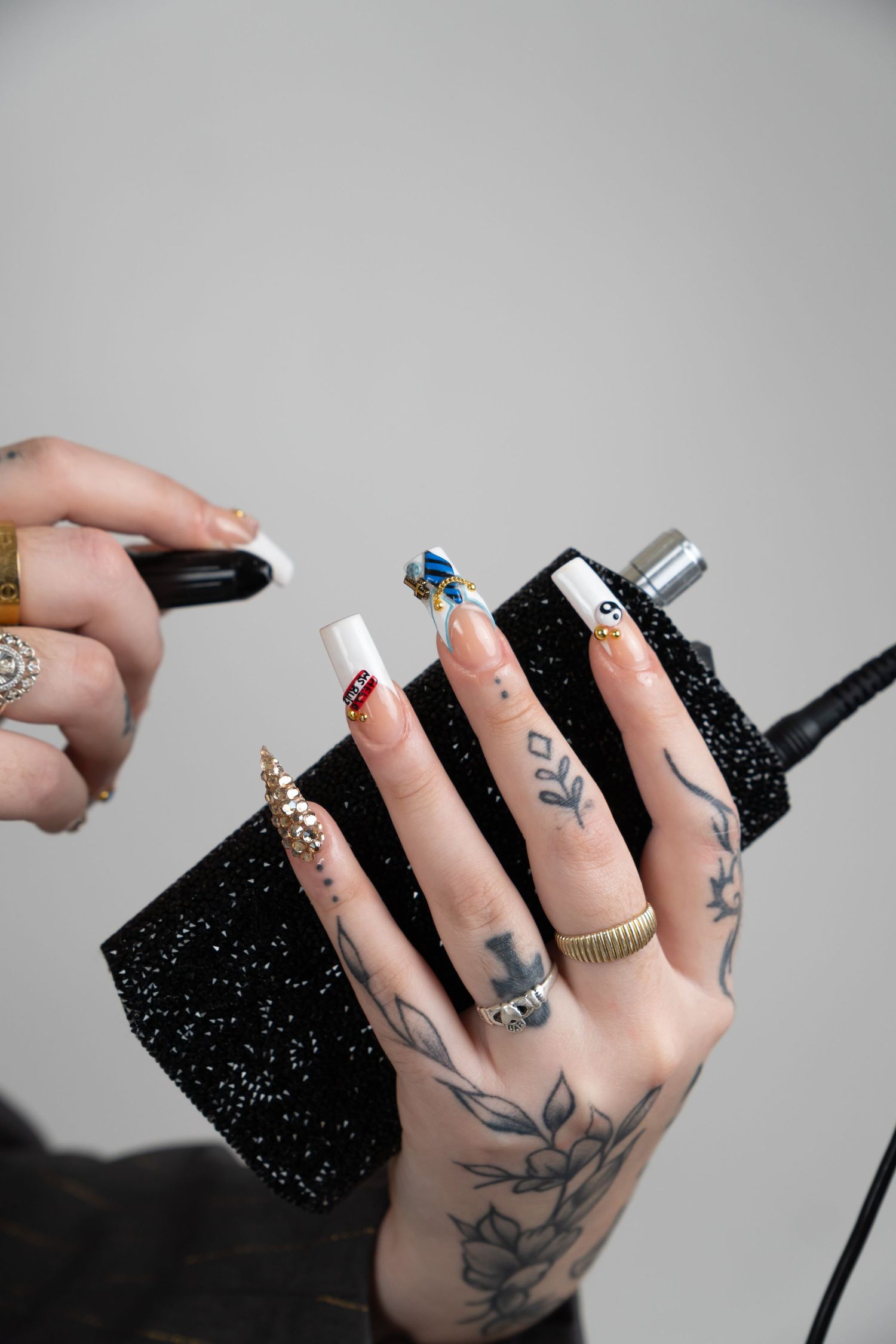 Tattooed hands with decorative long acrylic nails holding a black glittery bag near a microphone.
