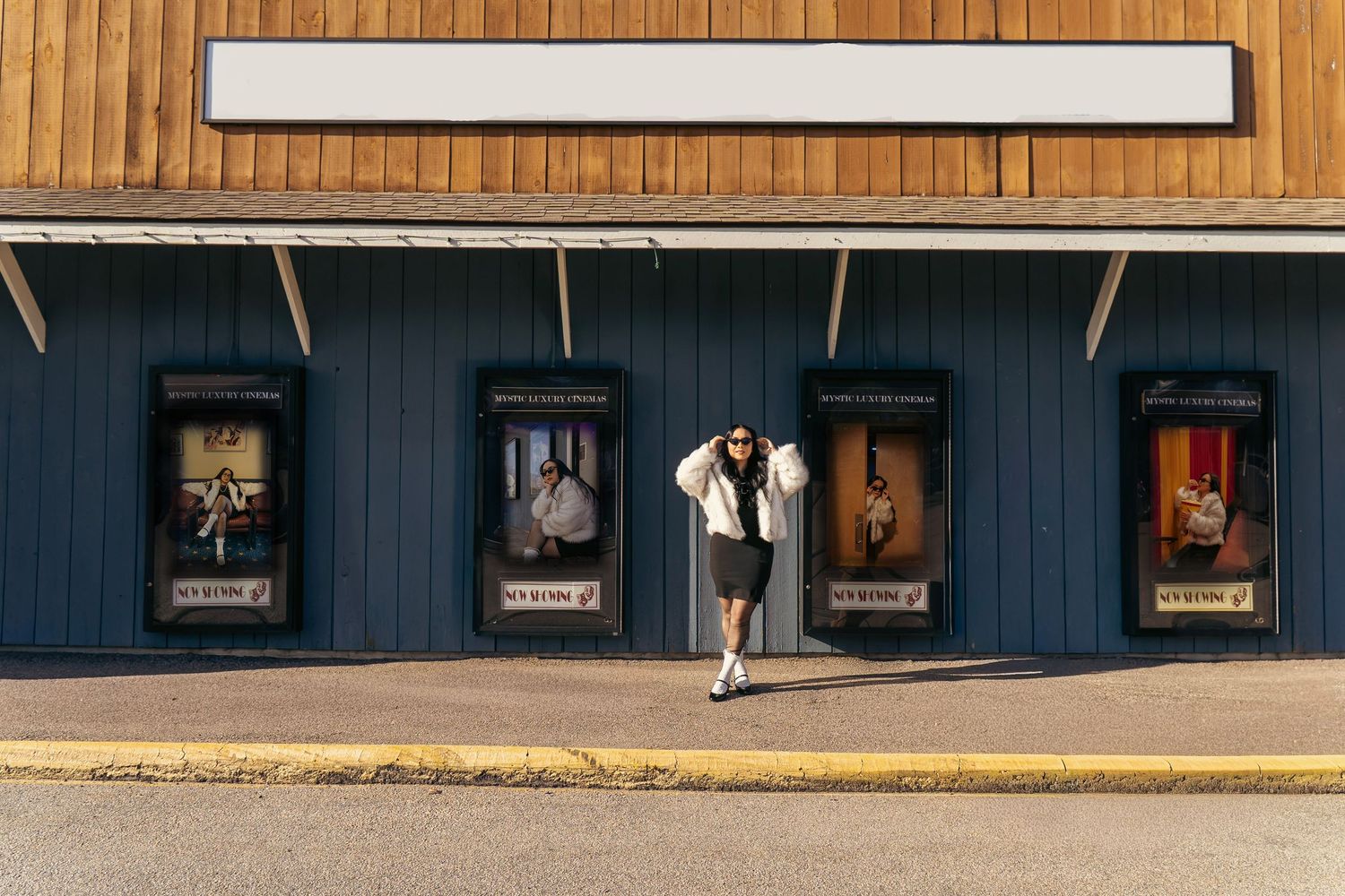 Woman posing outside a vintage theater with movie posters and a blank marquee sign on a sunny day.