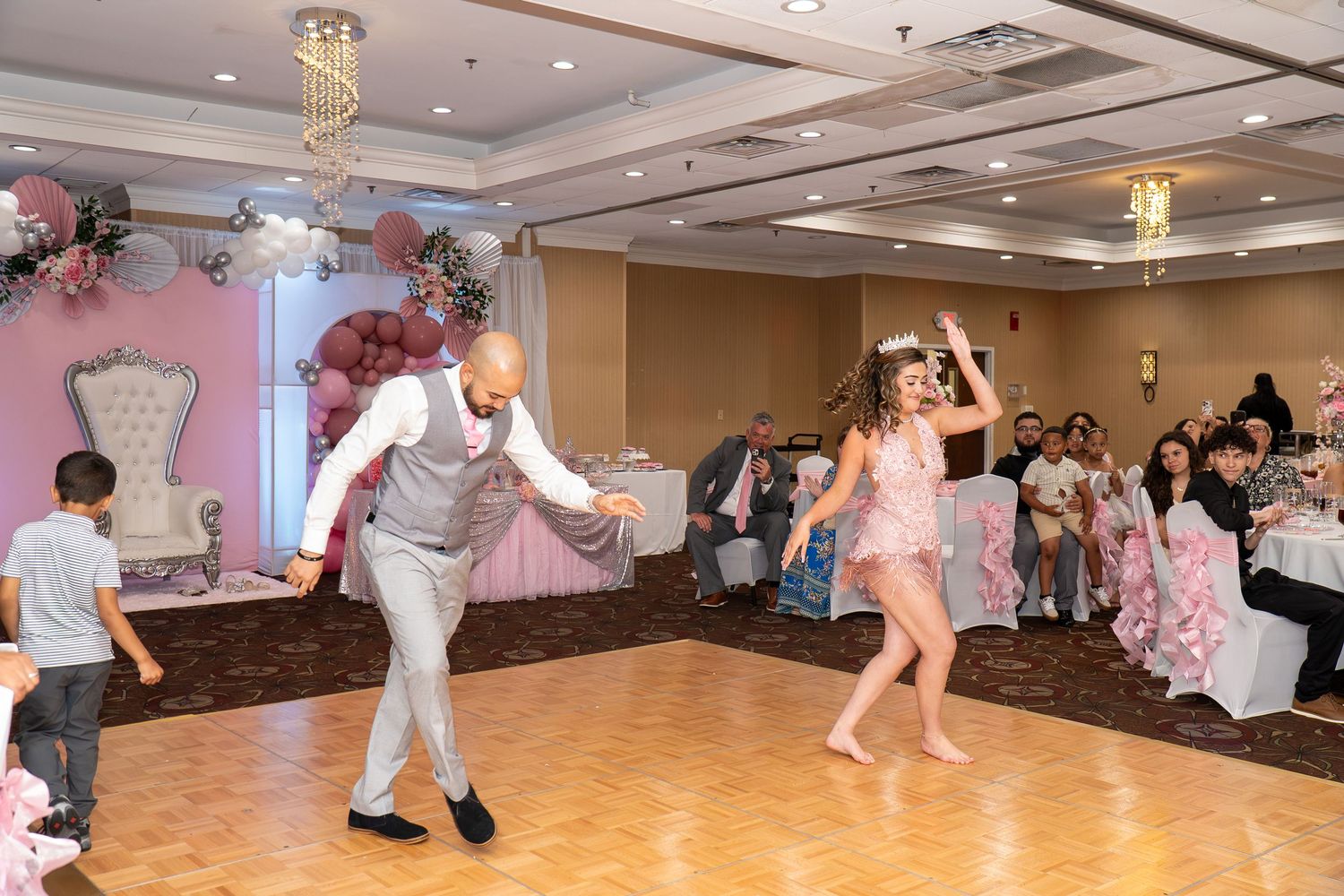 A man and woman dance energetically at an elegant quinceañera celebration in a decorated ballroom. Sweet 16!