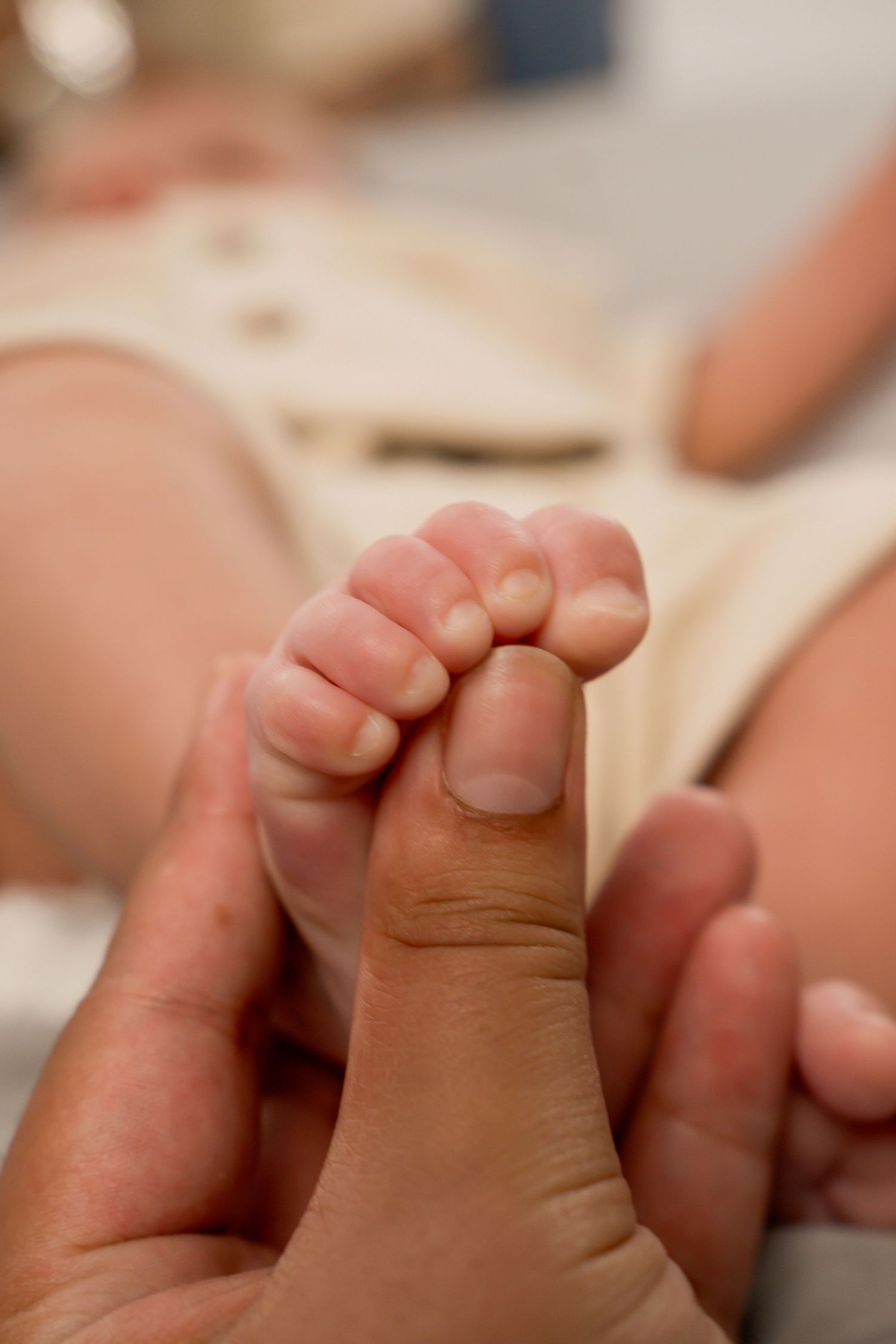 Close-up of a newborn baby's tiny hand gripping an adult's thumb, showing delicate fingers and nails. Newborn photoshoot.