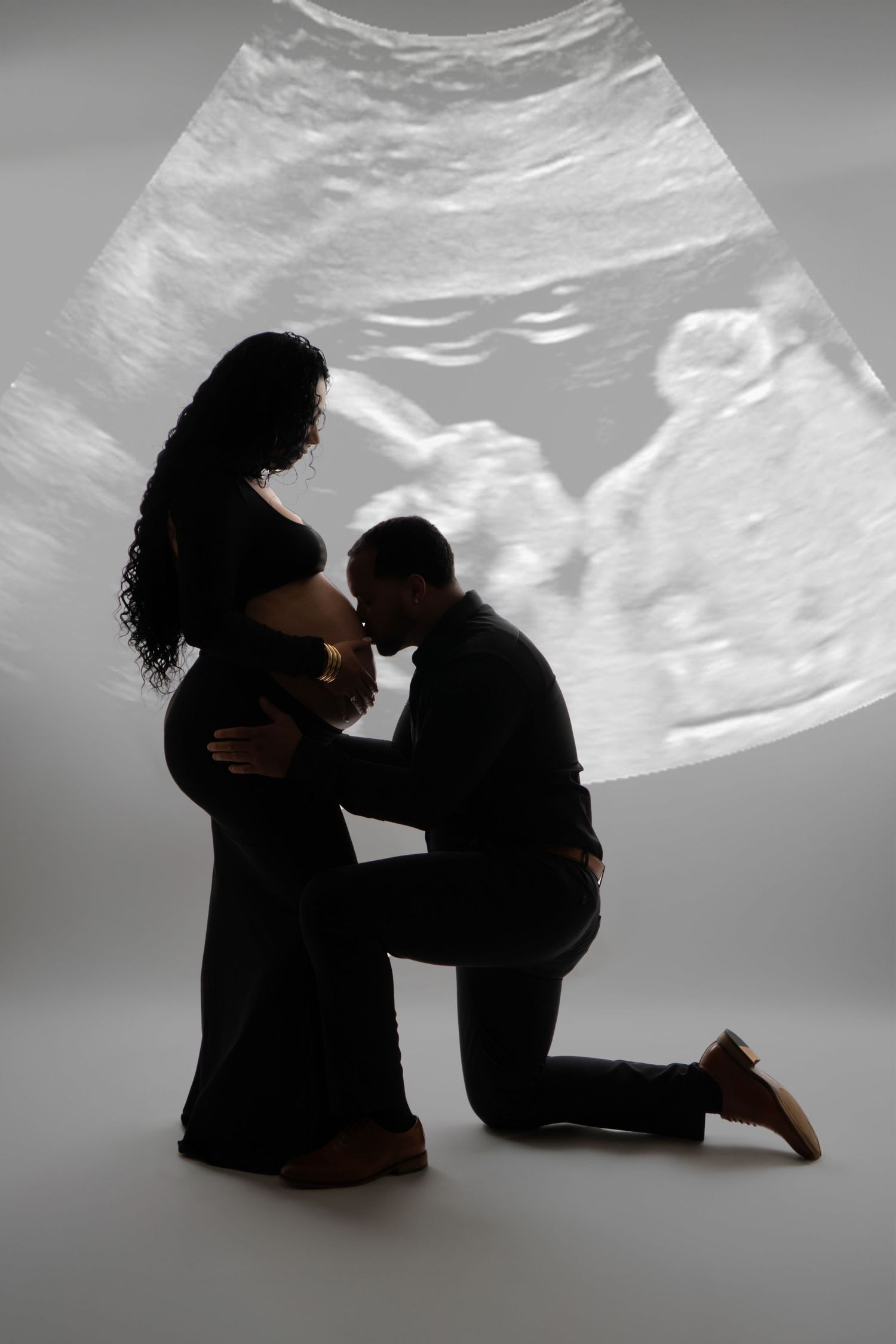 Silhouette of expectant couple with ultrasound image projected behind them on gray studio background.
