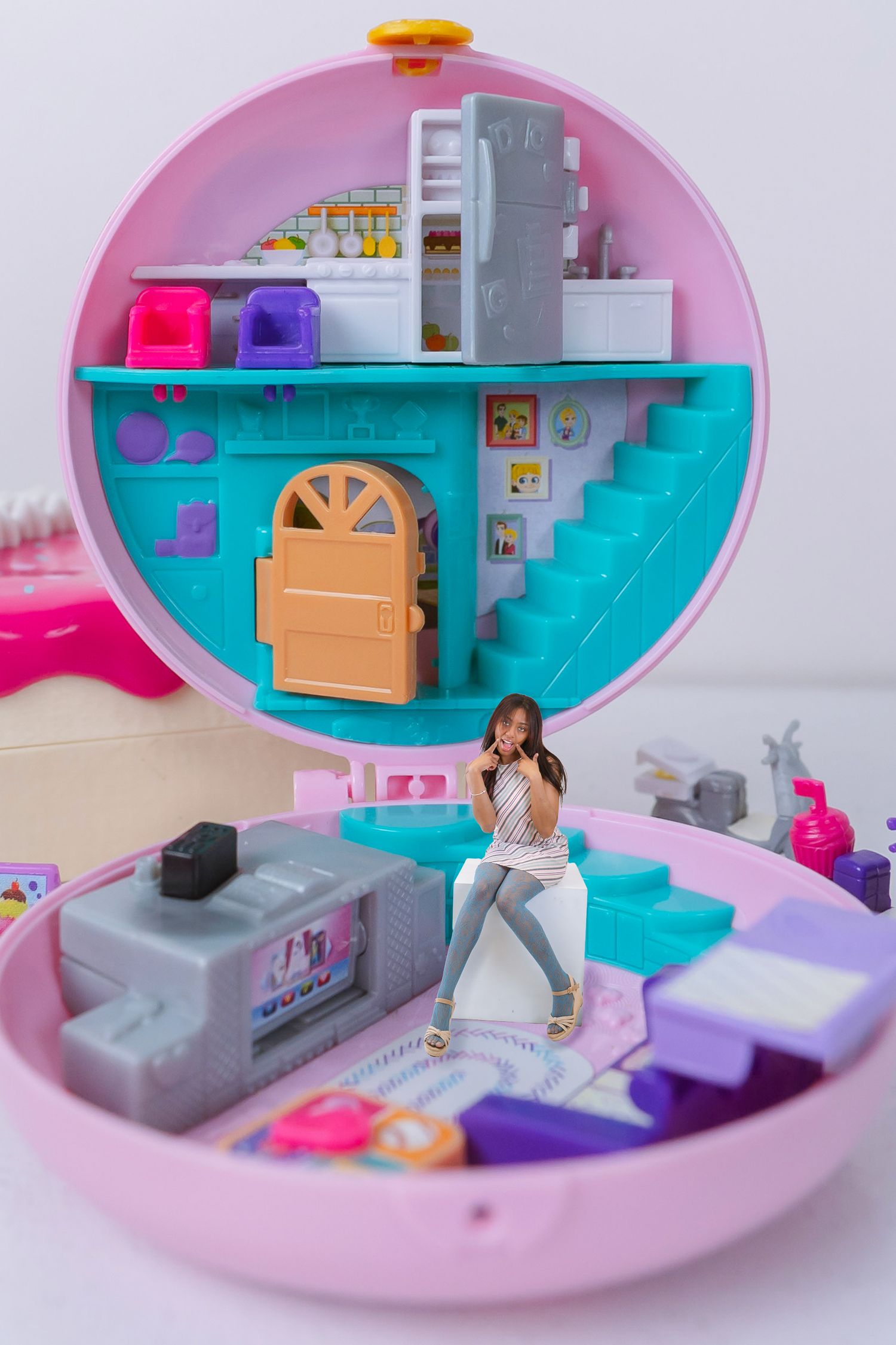 Polly Pocket pink compact playset open revealing a miniature dollhouse with a tiny doll figure, stairs, and colorful furniture.