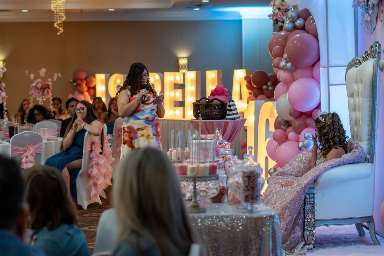 Guests gather around a decorated dessert table at Isabella's pink-themed quinceañera party. Sweet 16!