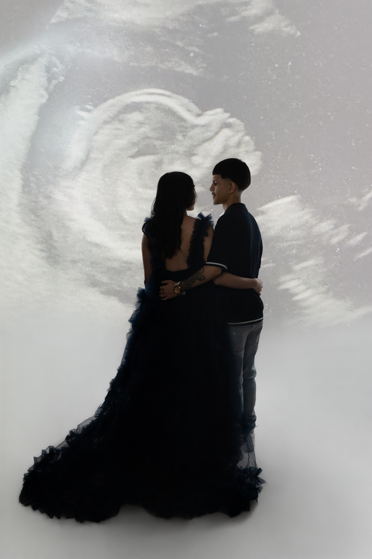 A couple in black attire embraces before a projected ultrasound image on a white background.