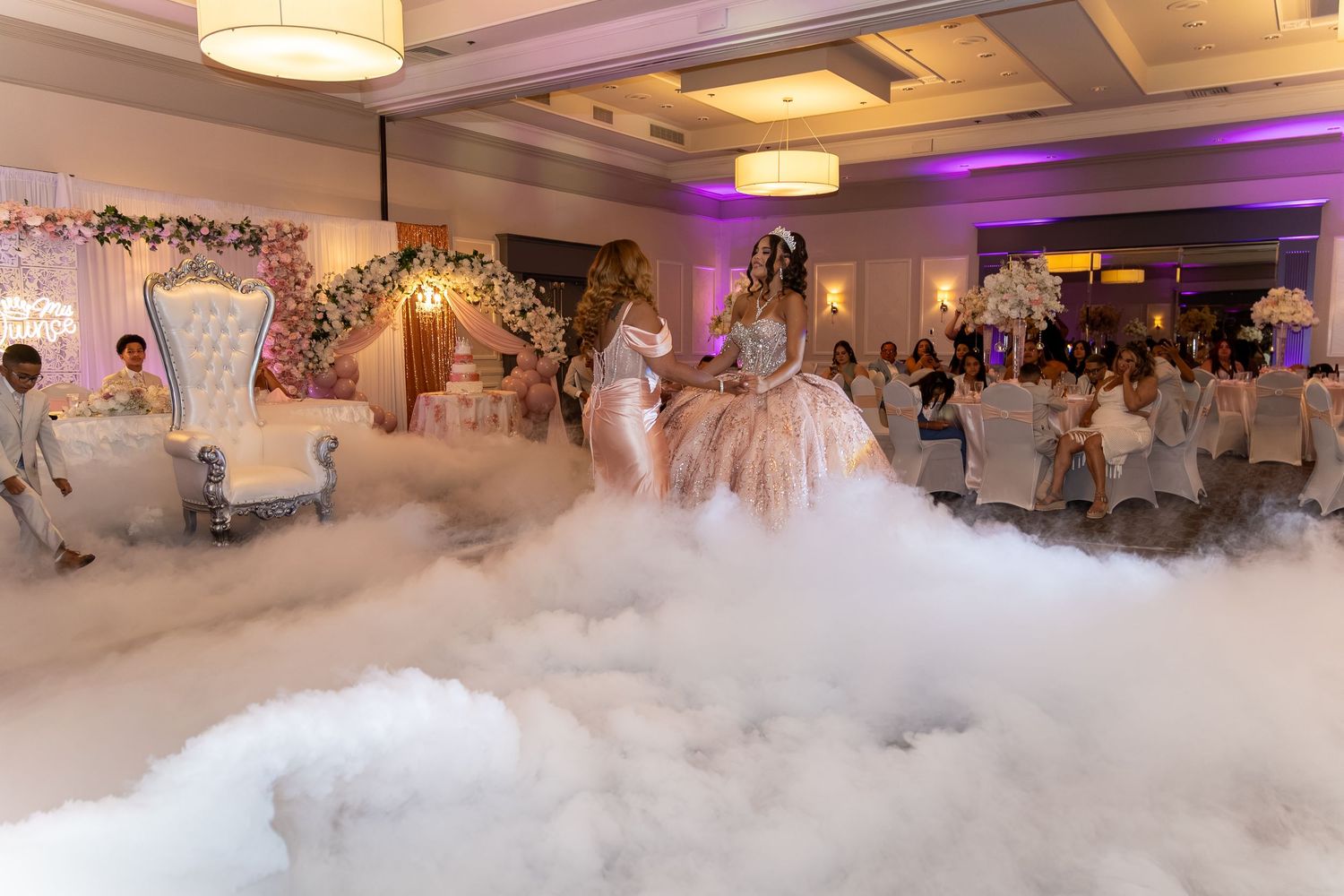 Quinceañera girl dances in ballgown amid dramatic dry ice fog in decorated banquet hall. Sweet 16/Quinceañera