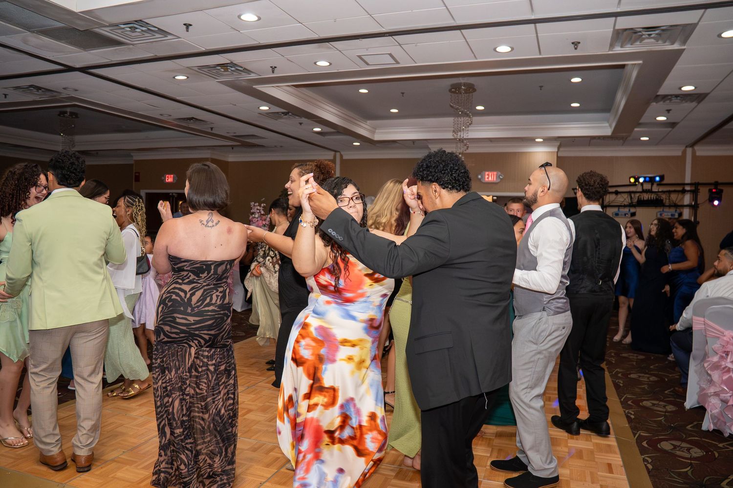 Guests dancing together at a wedding reception in a decorated ballroom venue. Sweet 16!