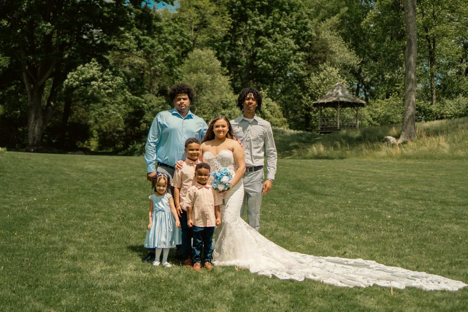 Bride and groom posing with family members on a green lawn at a wedding.