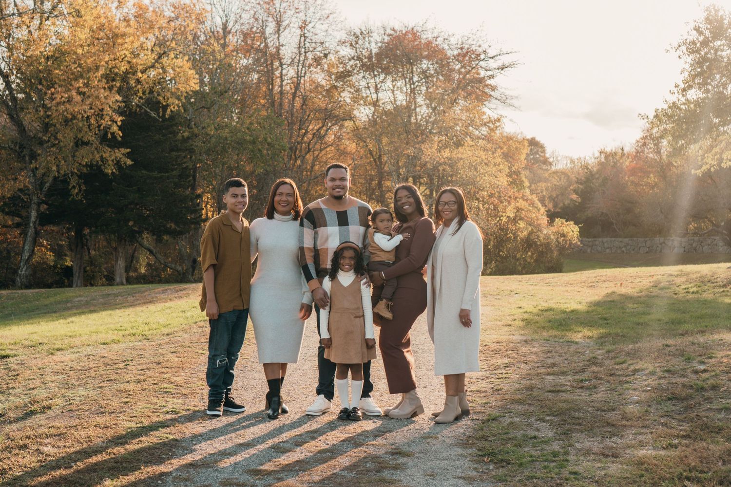 Multicultural family of seven poses together in autumn park with golden trees at sunset.
