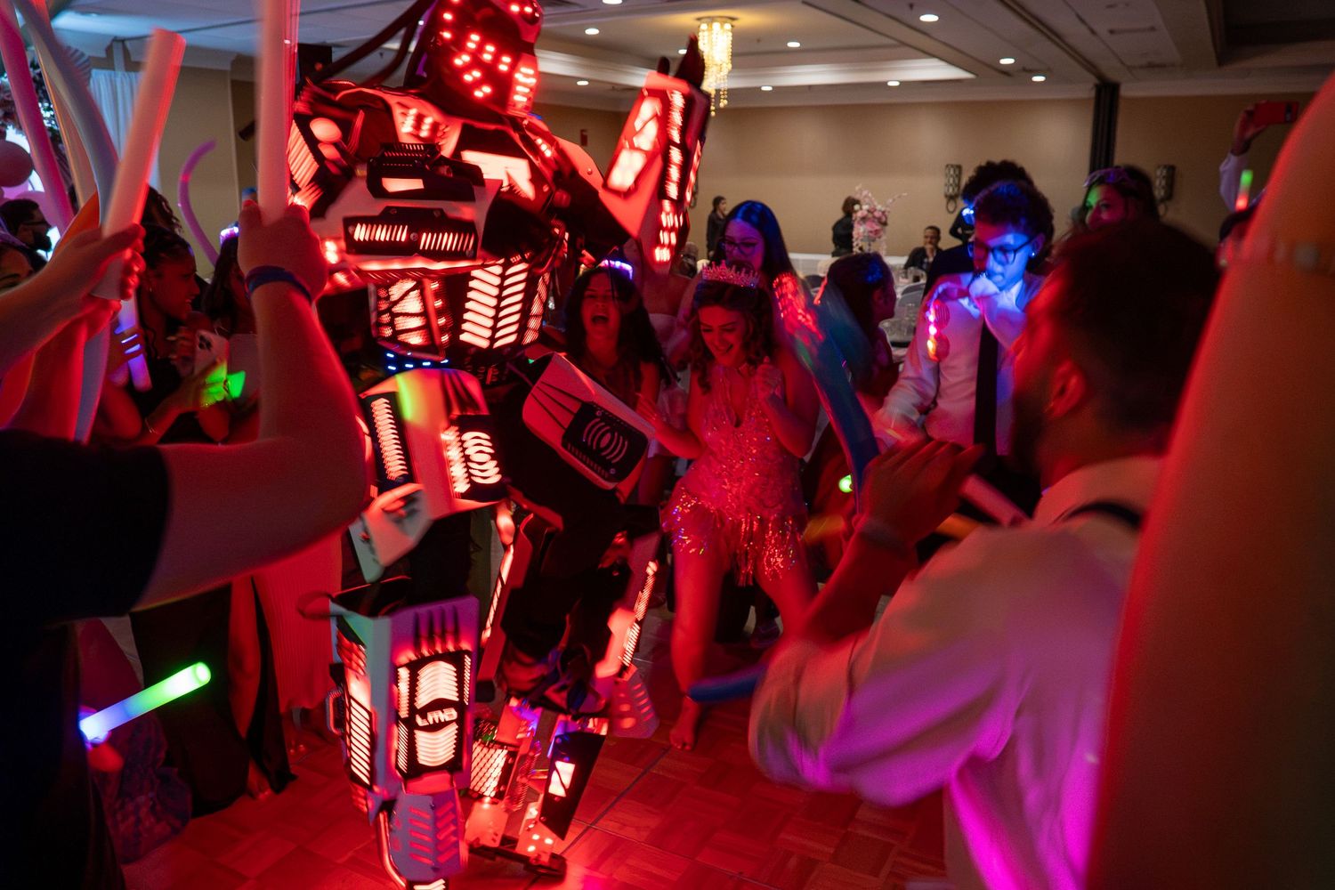 Party guests dance alongside a large illuminated LED robot at a vibrant quinceañera event. Sweet 16!