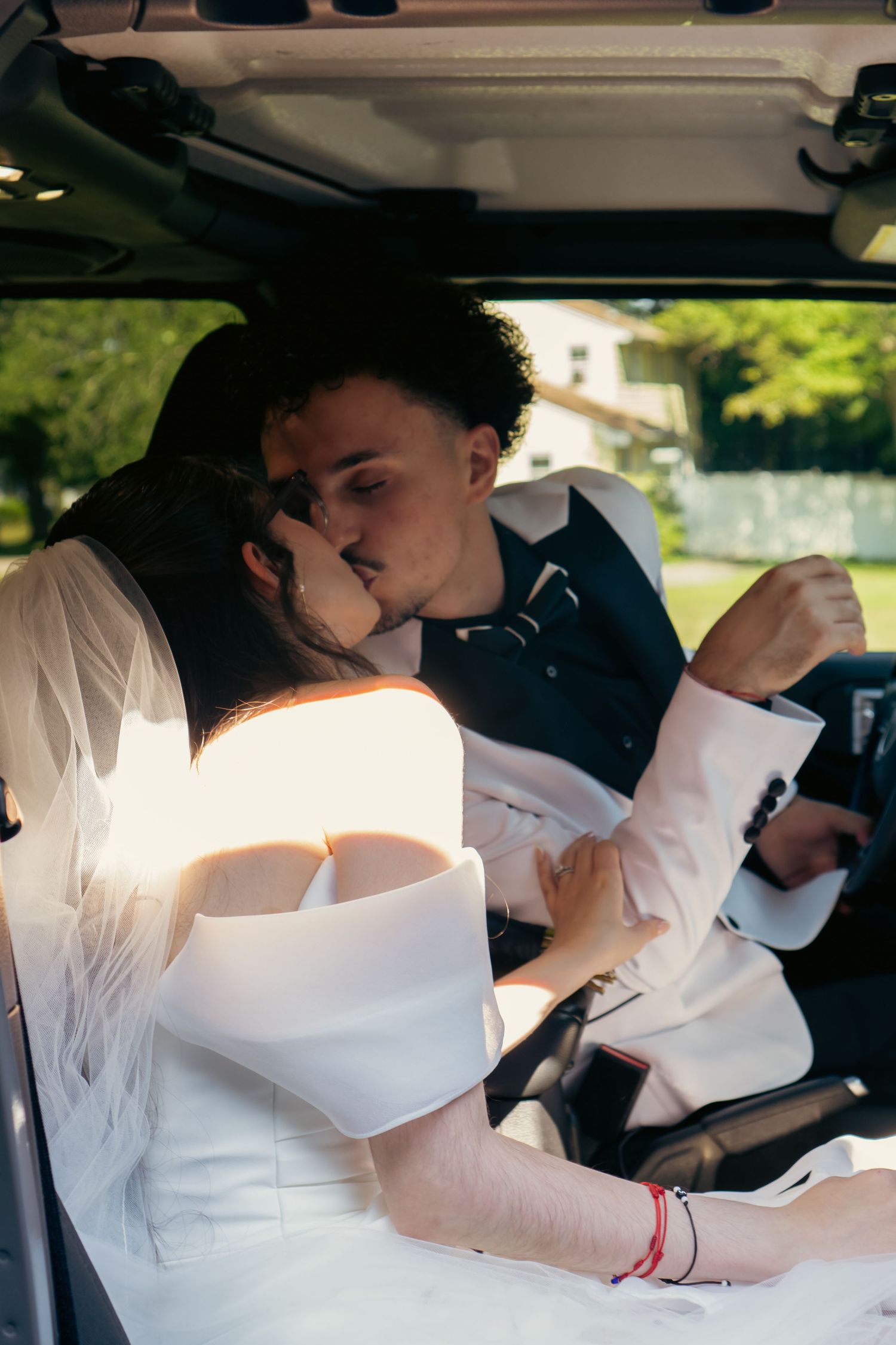 Bride and groom sharing a romantic kiss inside a car on their wedding day.