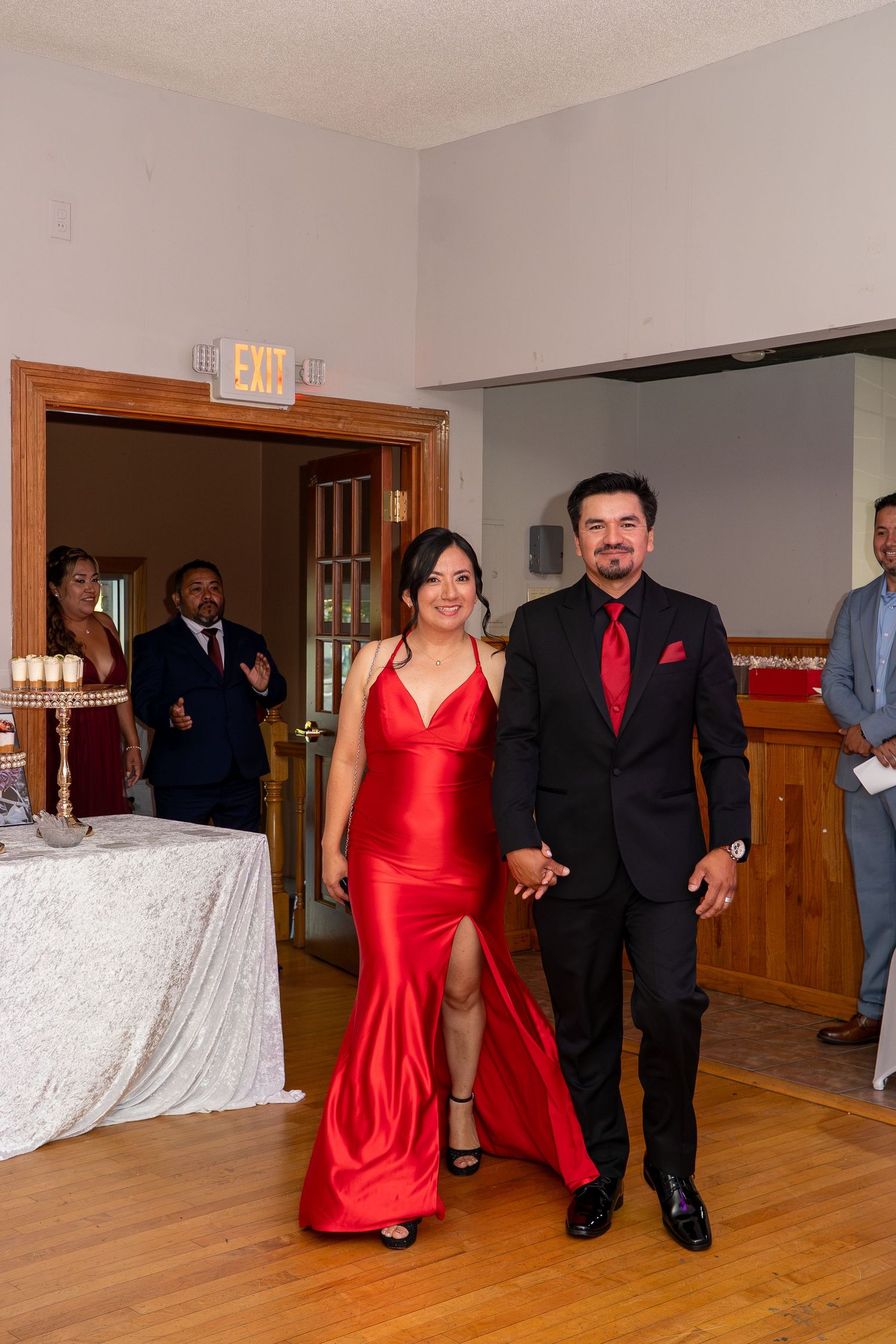 Couple in matching red and black formal attire holding hands making grand entrance at elegant wedding reception.