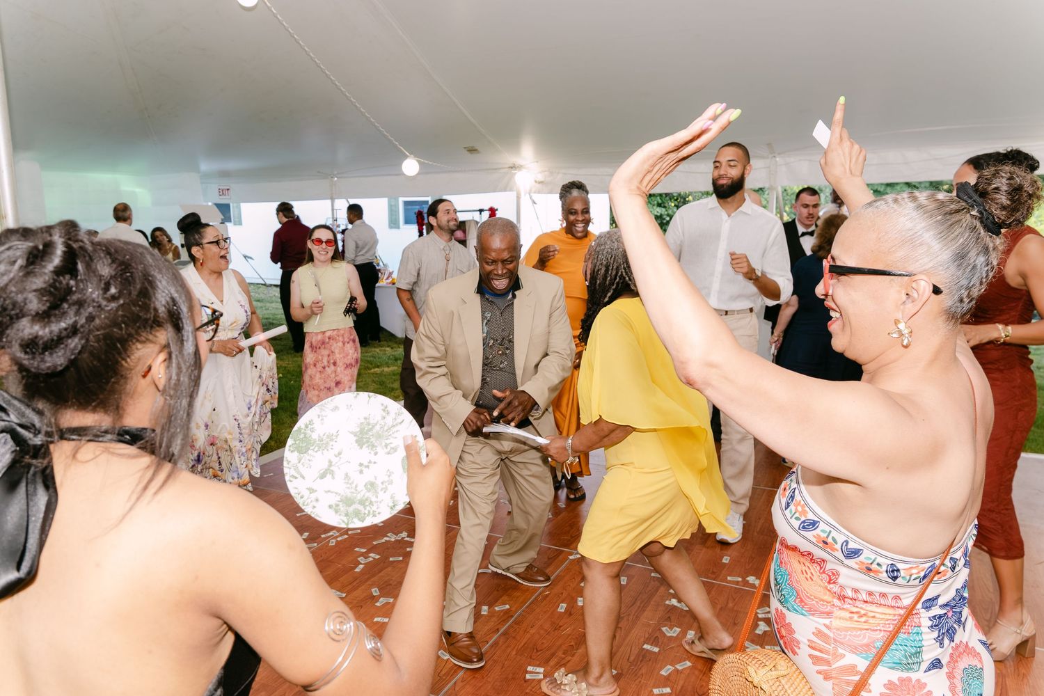 Guests dancing and celebrating at an outdoor wedding reception under a white tent with festive decorations.