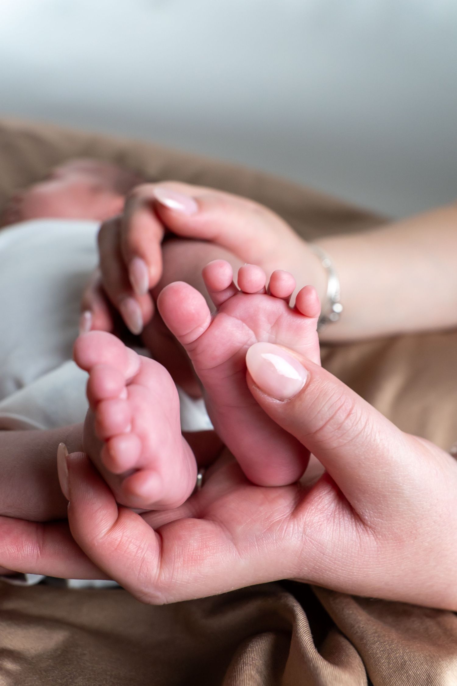 Adult hands gently cradling tiny newborn baby feet in a soft, tender close-up photo.