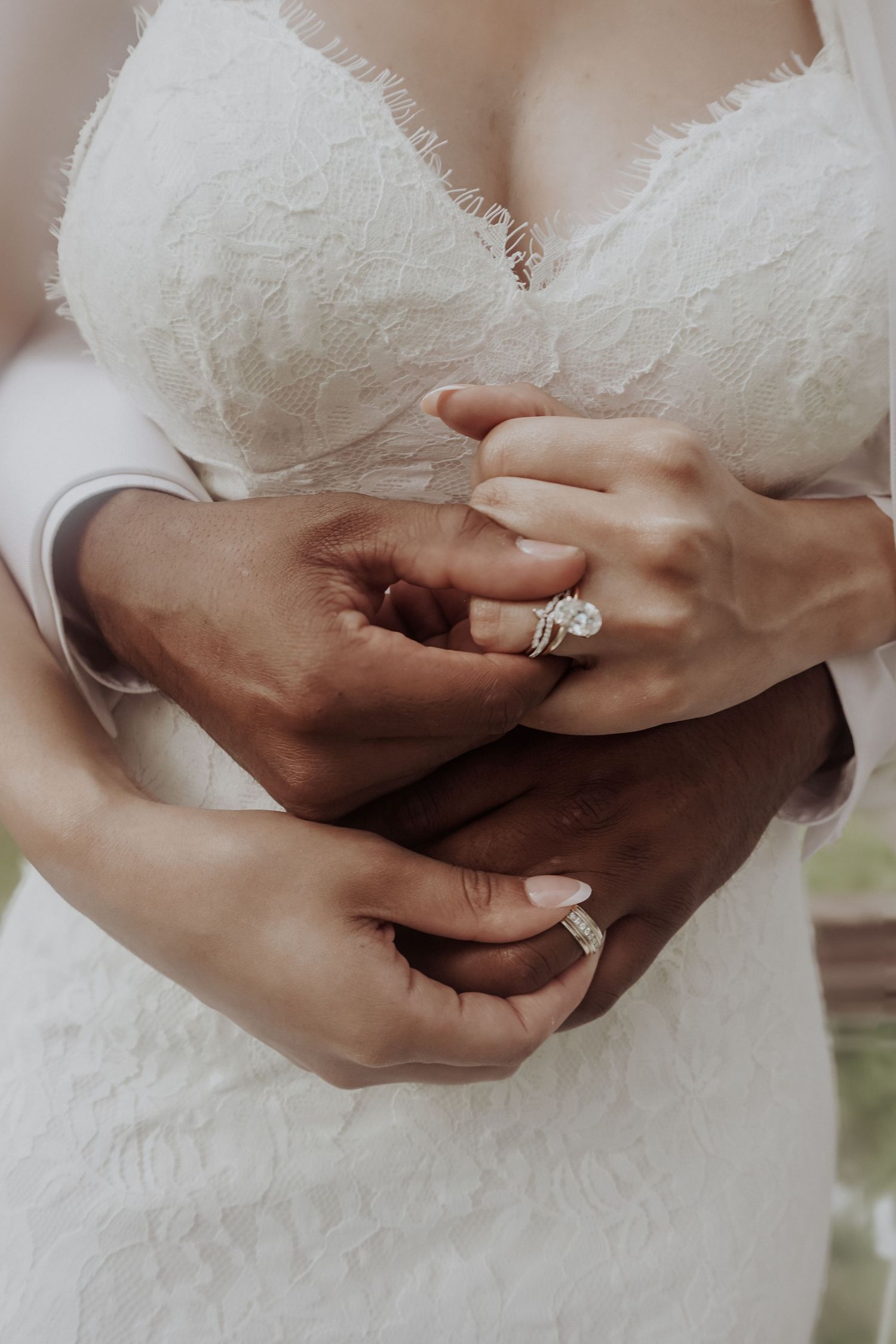 Close-up of bride and groom holding hands showing diamond engagement ring and wedding band on their wedding day.