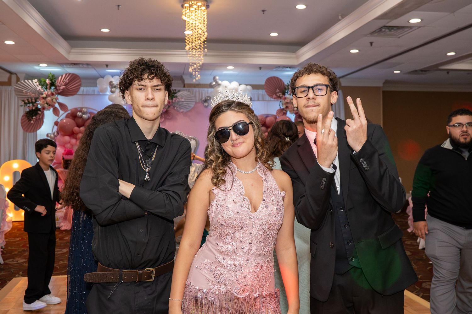 Three teens posing at a formal quinceañera party with pink floral decor. Sweet 16!