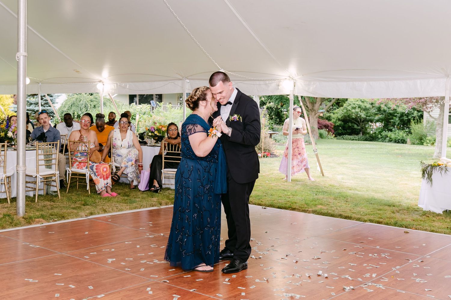 Mother and groom share an emotional first dance under a white tent at an outdoor wedding reception.