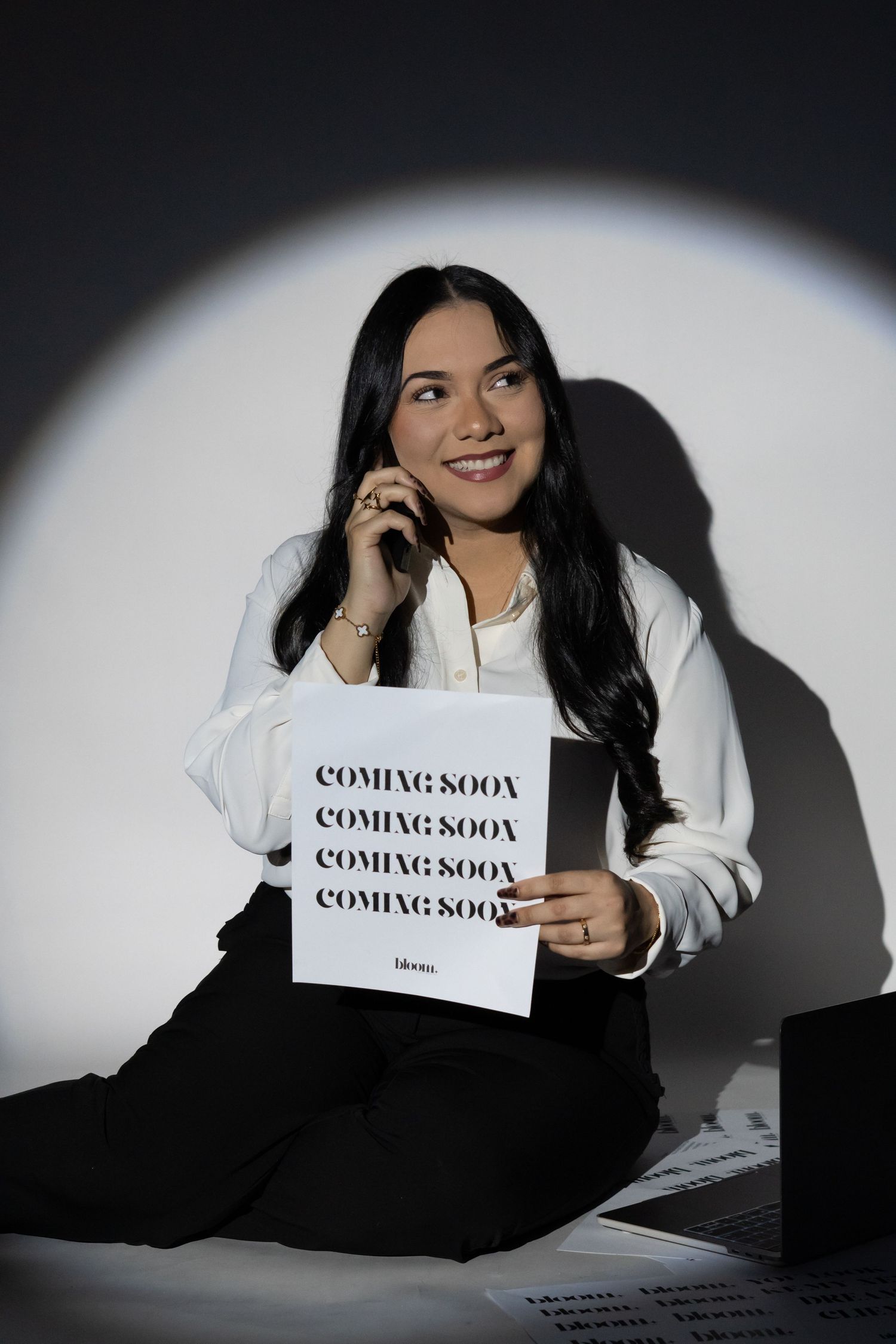 Smiling businesswoman holding coming soon sign while talking on phone in dramatic spotlight.