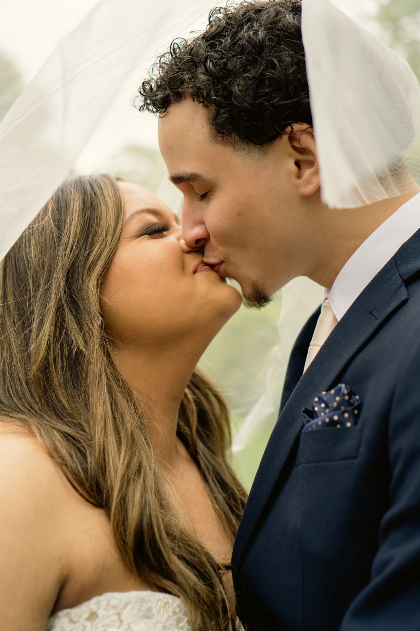 Bride and groom kissing under a veil in an outdoor wedding photo.