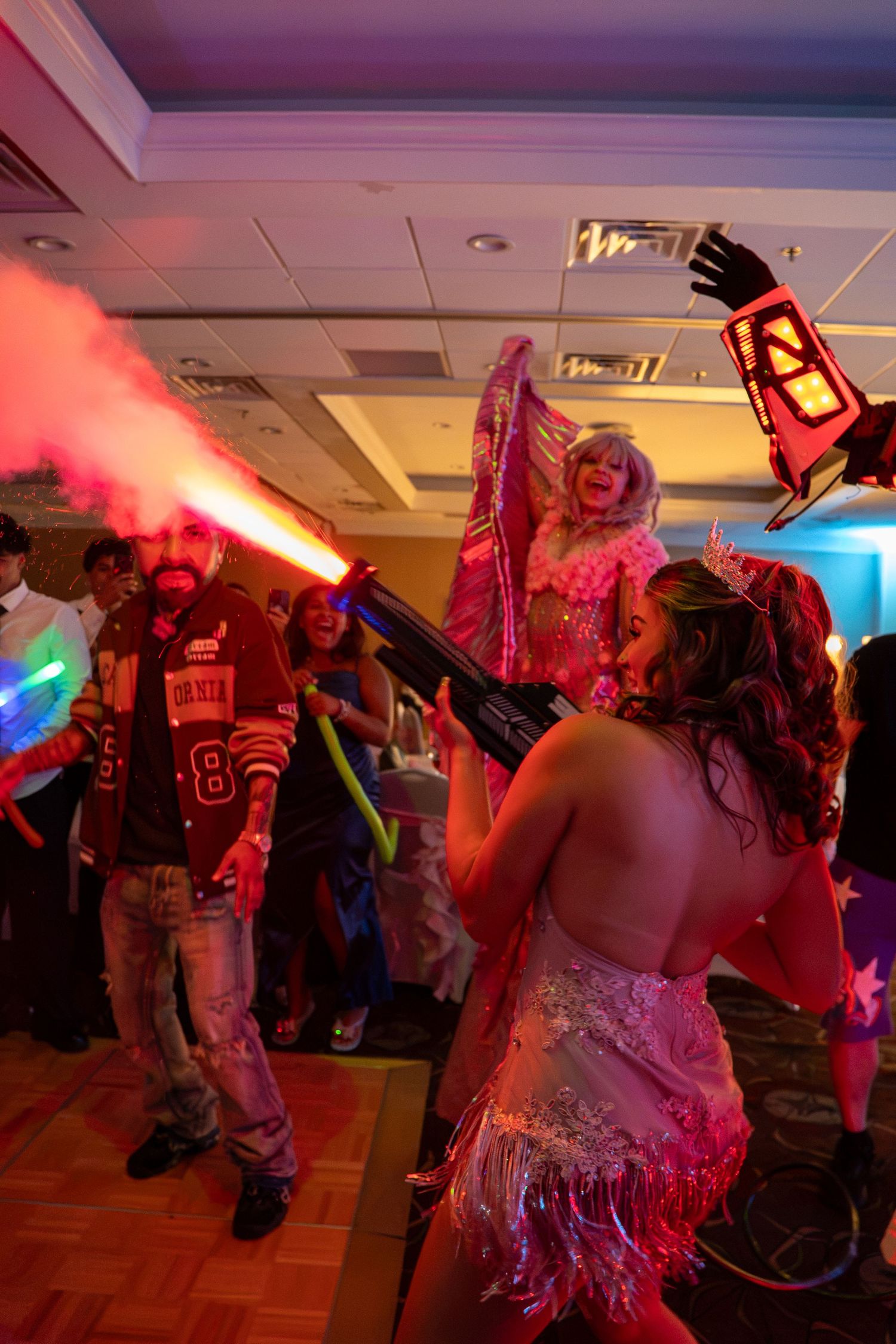Colorful party scene with performers, fog machine, stilt walker, and glowing props in a festive ballroom celebration. Sweet 16!