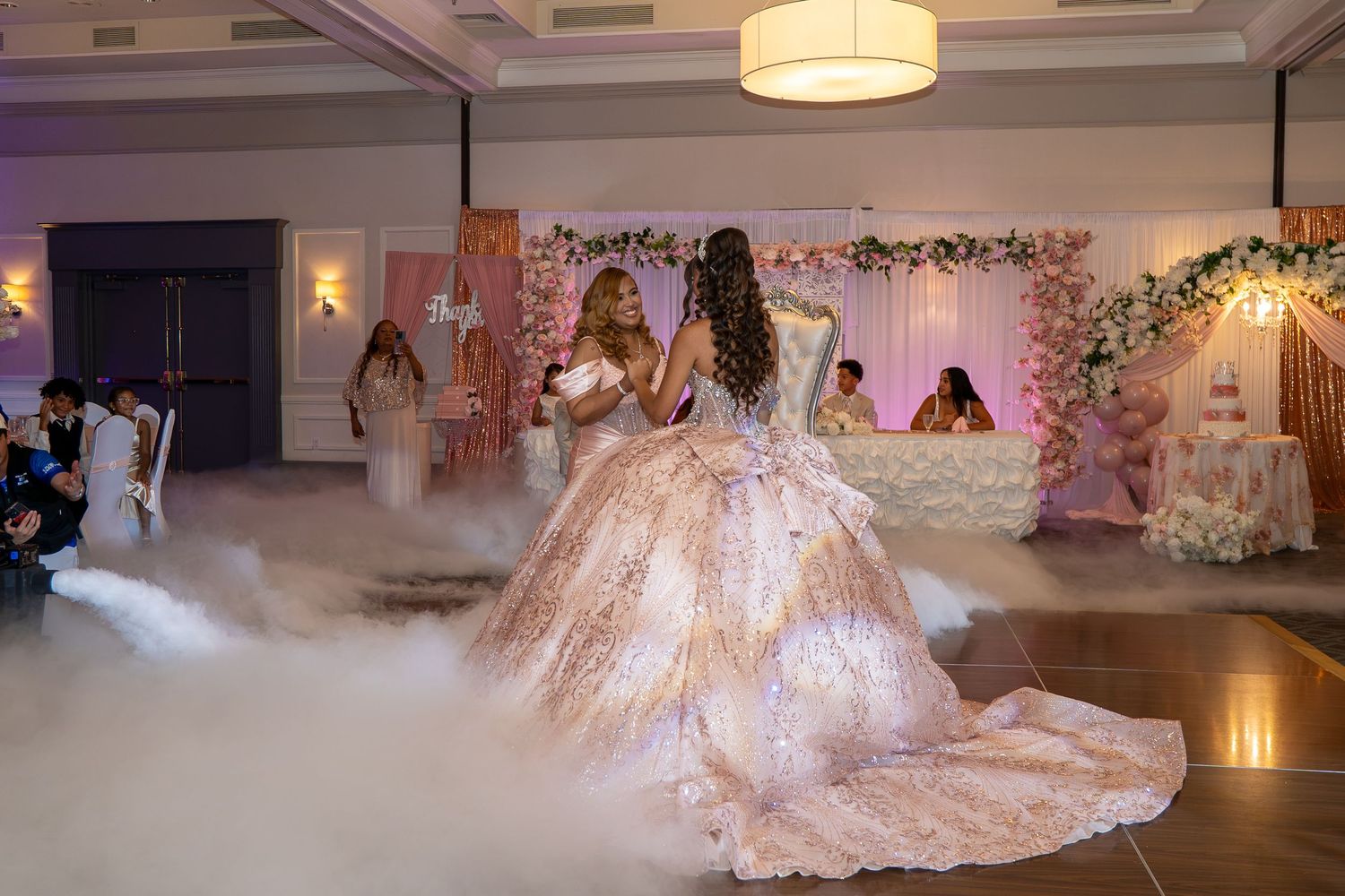 Elegant quinceañera celebration with girl in pink ballgown dancing on foggy floor at decorated venue. Sweet 16/Quinceañera